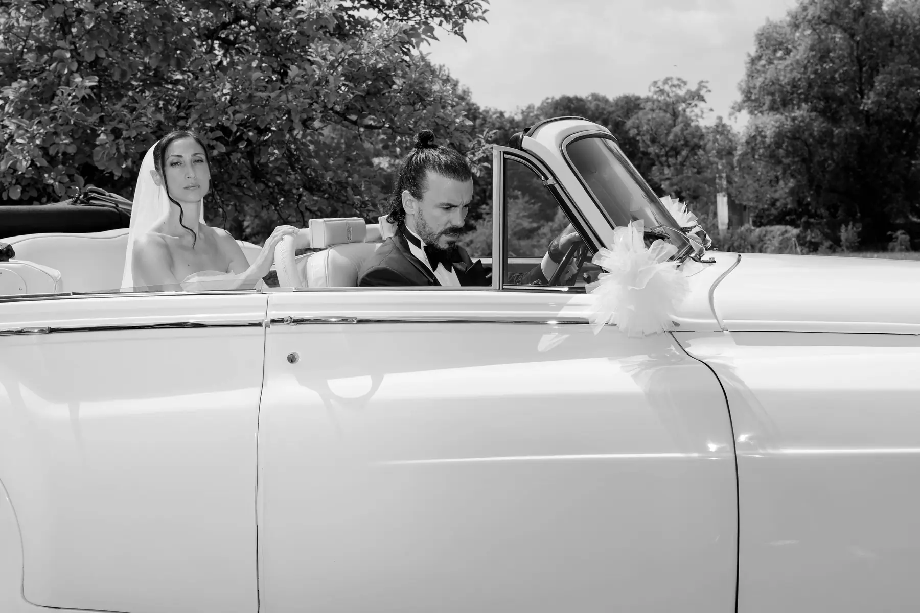 Bride and groom in a white vintage Rolls-Royce convertible, black and white