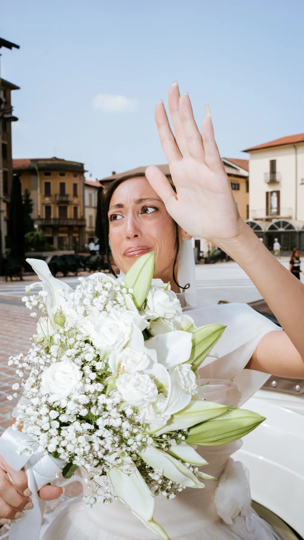 Bride waving from the car with her white bouquet in an Italian town square