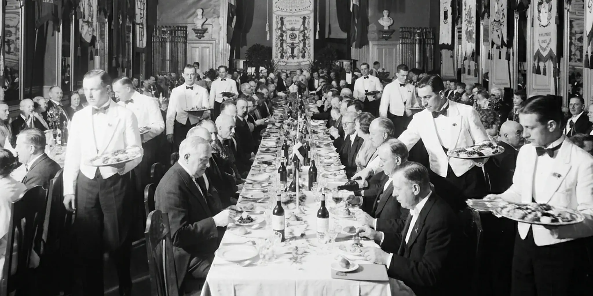 Waiters in white jackets serving a long banquet table