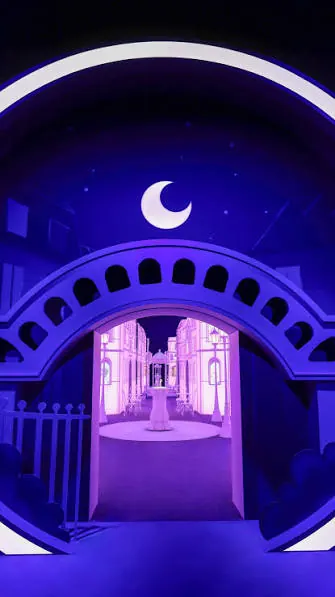 Illuminated arch with a crescent moon opening onto a violet lit street set installation