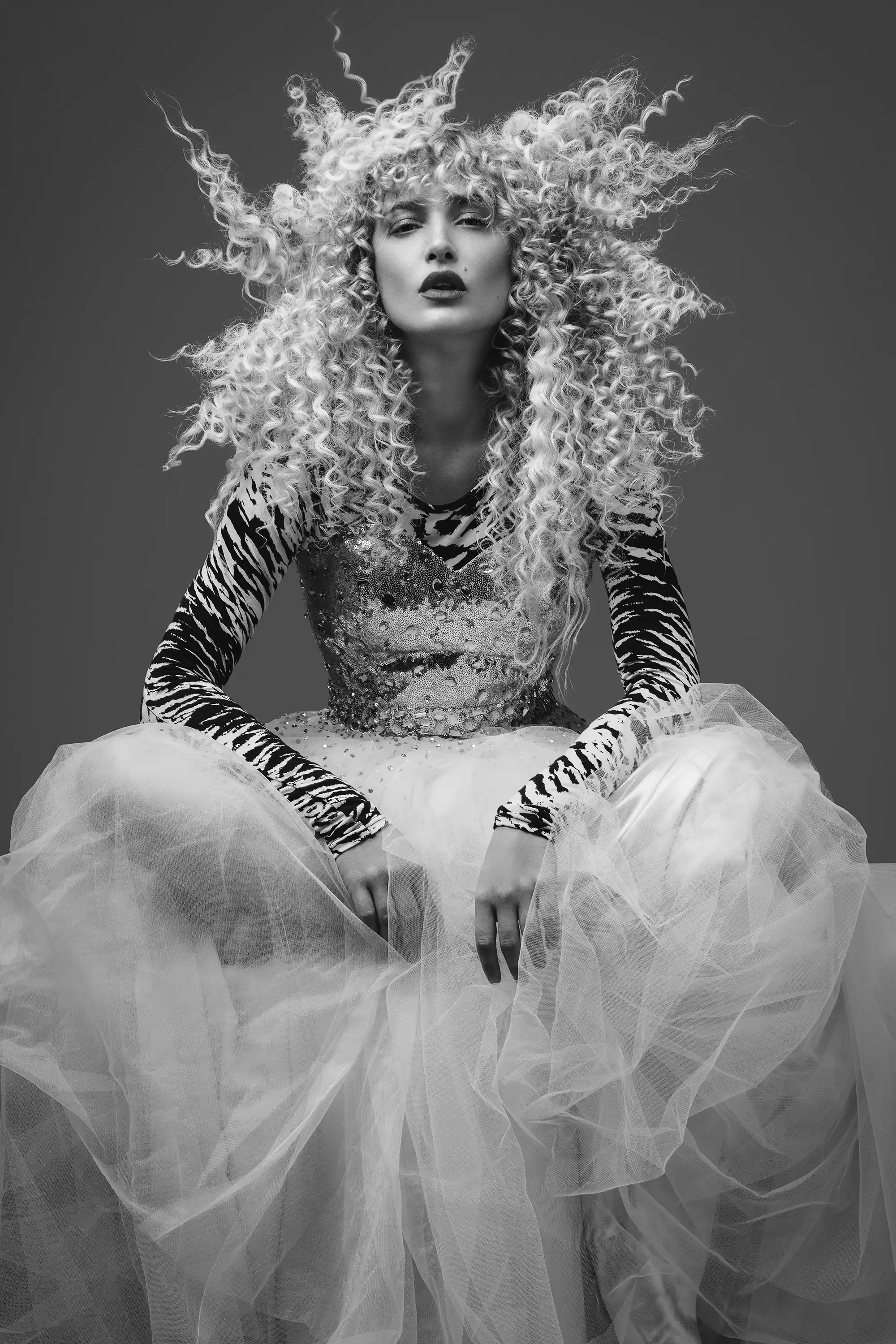 Dramatic curly-haired hairdresser talent in zebra top and tulle skirt for Coverpage Dubai showcase.
