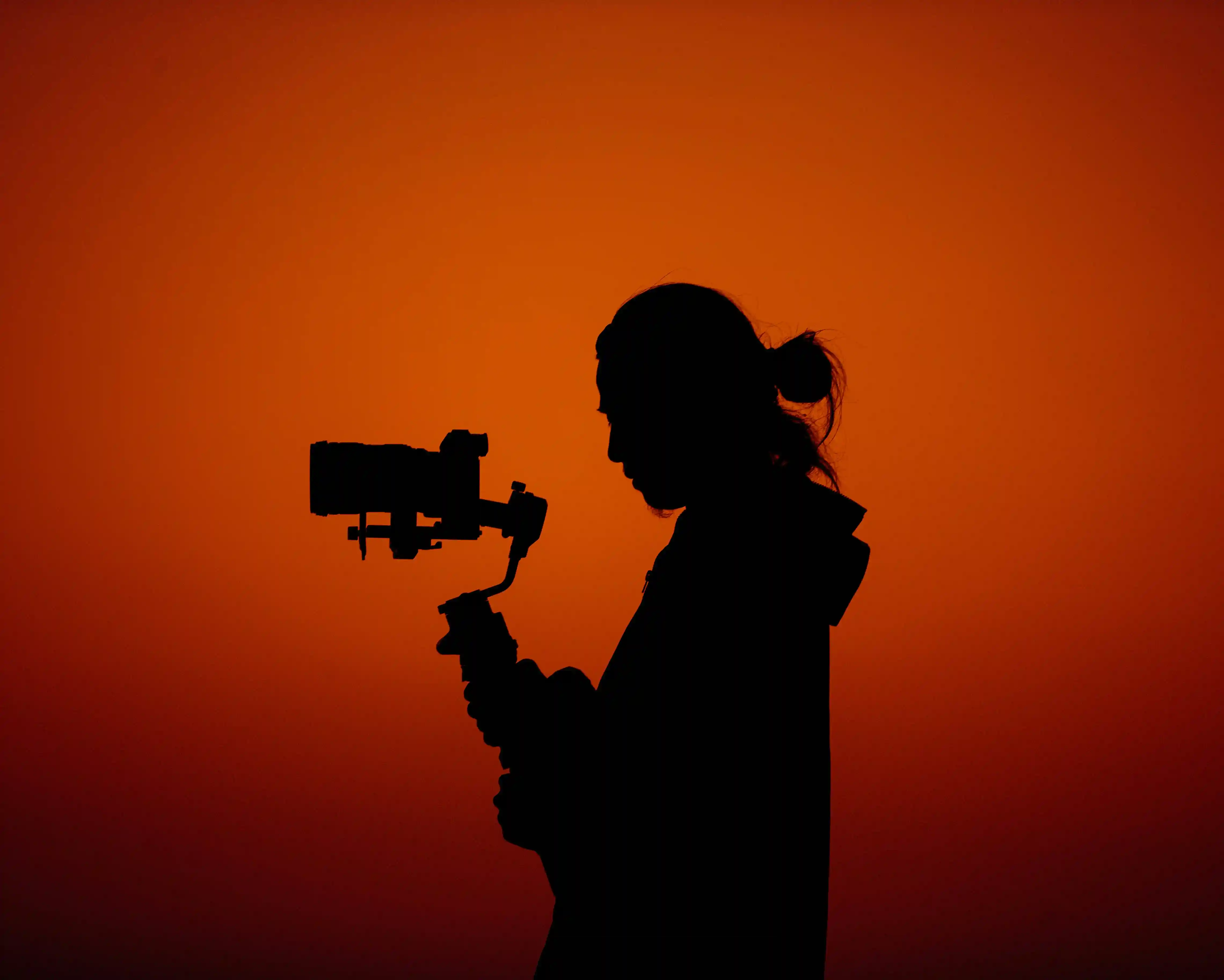 Silhouette of videographer talent holding gimbal camera against orange sunset for Coverpage Dubai luxury event agency.