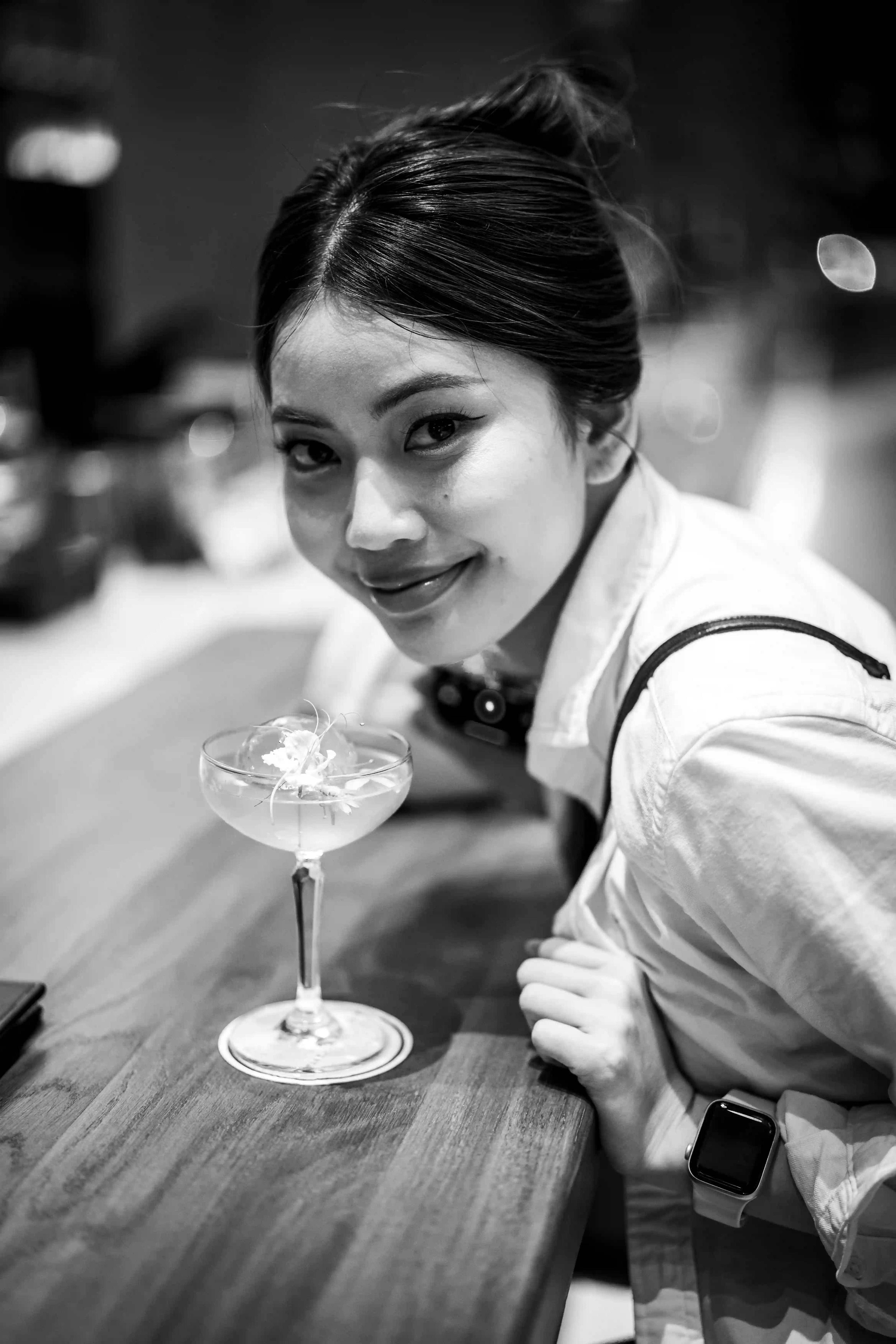 Elegant bartender talent smiling with flower cocktail glass in black and white bar portrait for Coverpage Dubai luxury agency.