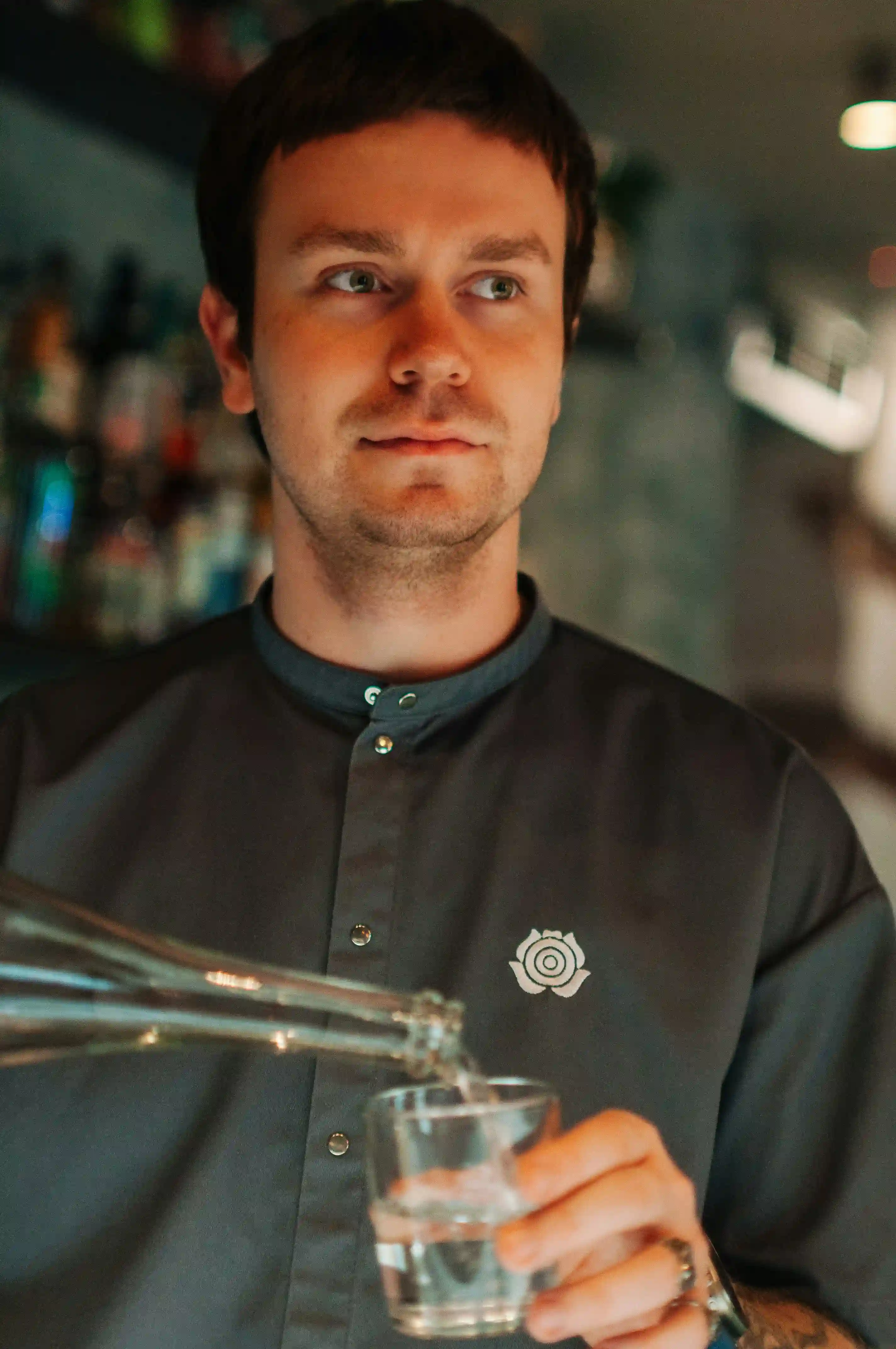 Professional bartender talent pouring clear drink from double spout into glass at bar for Coverpage Dubai agency.