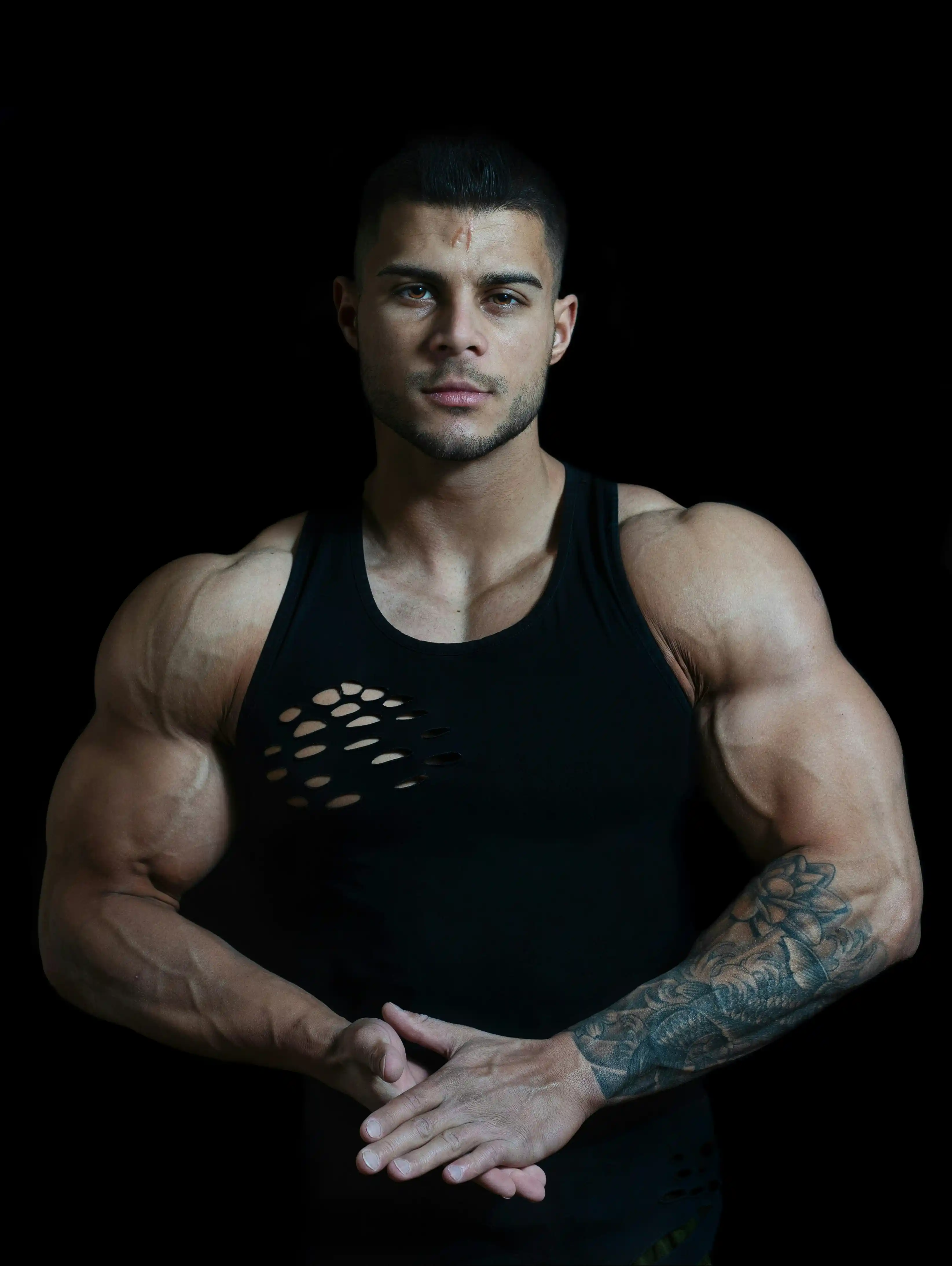 Cover Page elite bodyguard with tattooed arm, imposing physique in black ripped tank top, arms crossed on dark background.