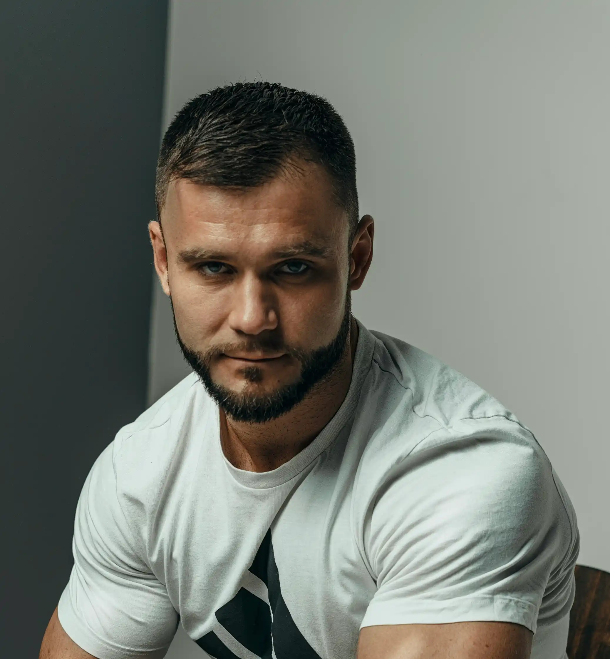 Professional security agent from Cover Page agency, muscular build in white Adidas t-shirt, intense gaze on gray background.