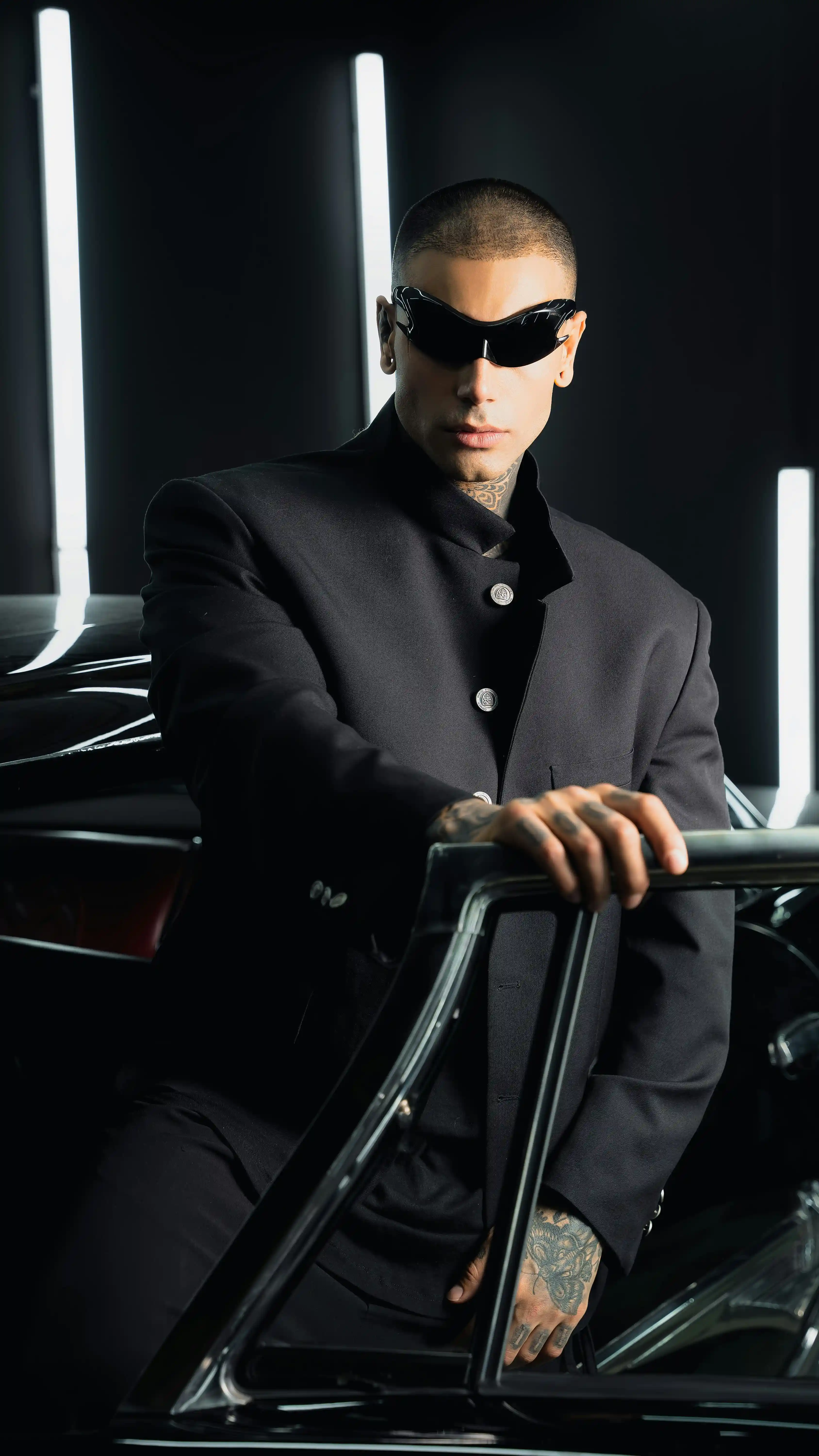 lite Cover Page bodyguard in black suit and futuristic sunglasses, tattooed neck and hand, leaning on luxury car door.