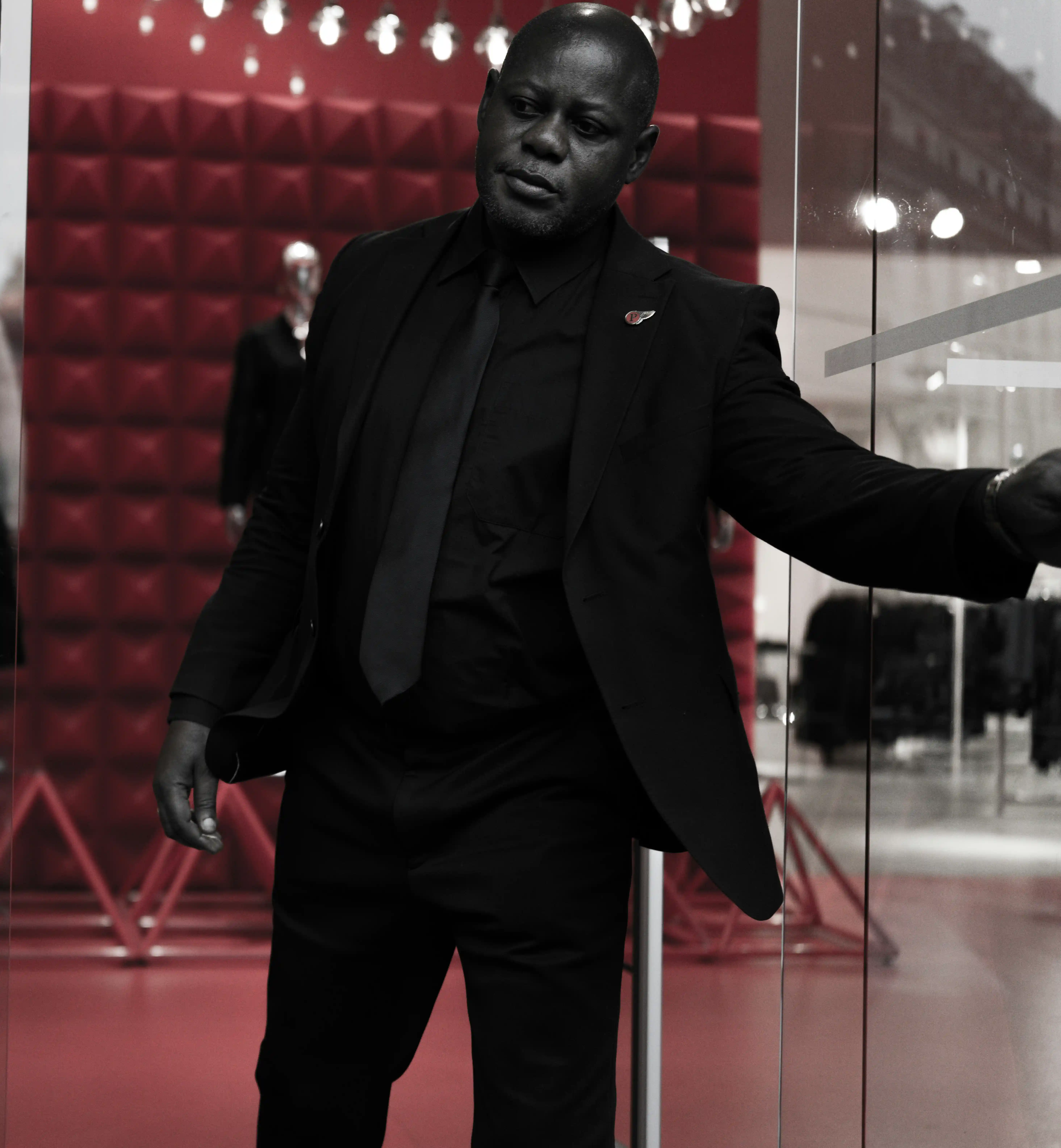 Cover Page elite security personnel in black suit and tie, extending arm in alert pose, in red event hall setting.