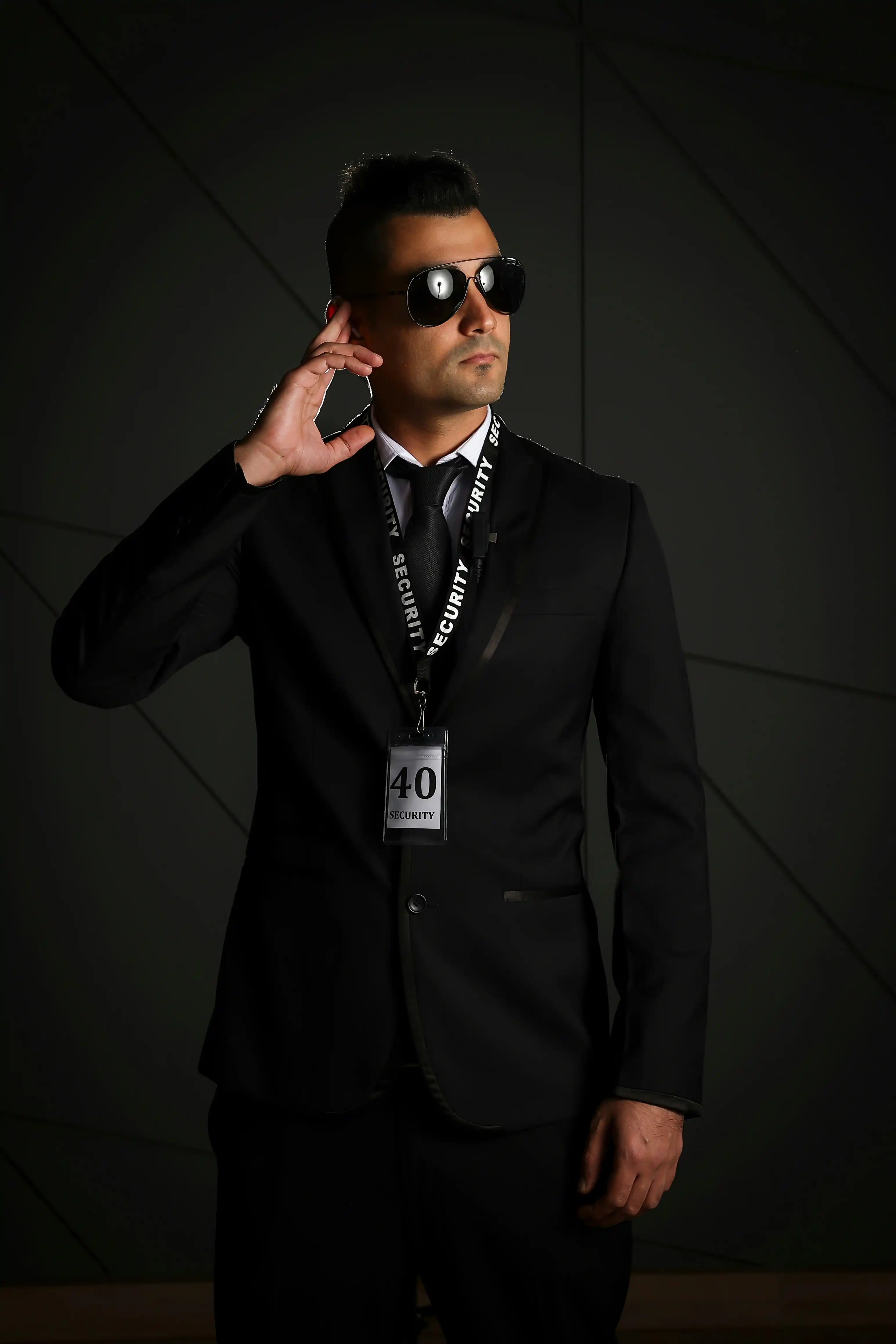Cover Page professional security guard in black suit and sunglasses, touching earpiece with SECURITY lanyard and badge, on dark background.