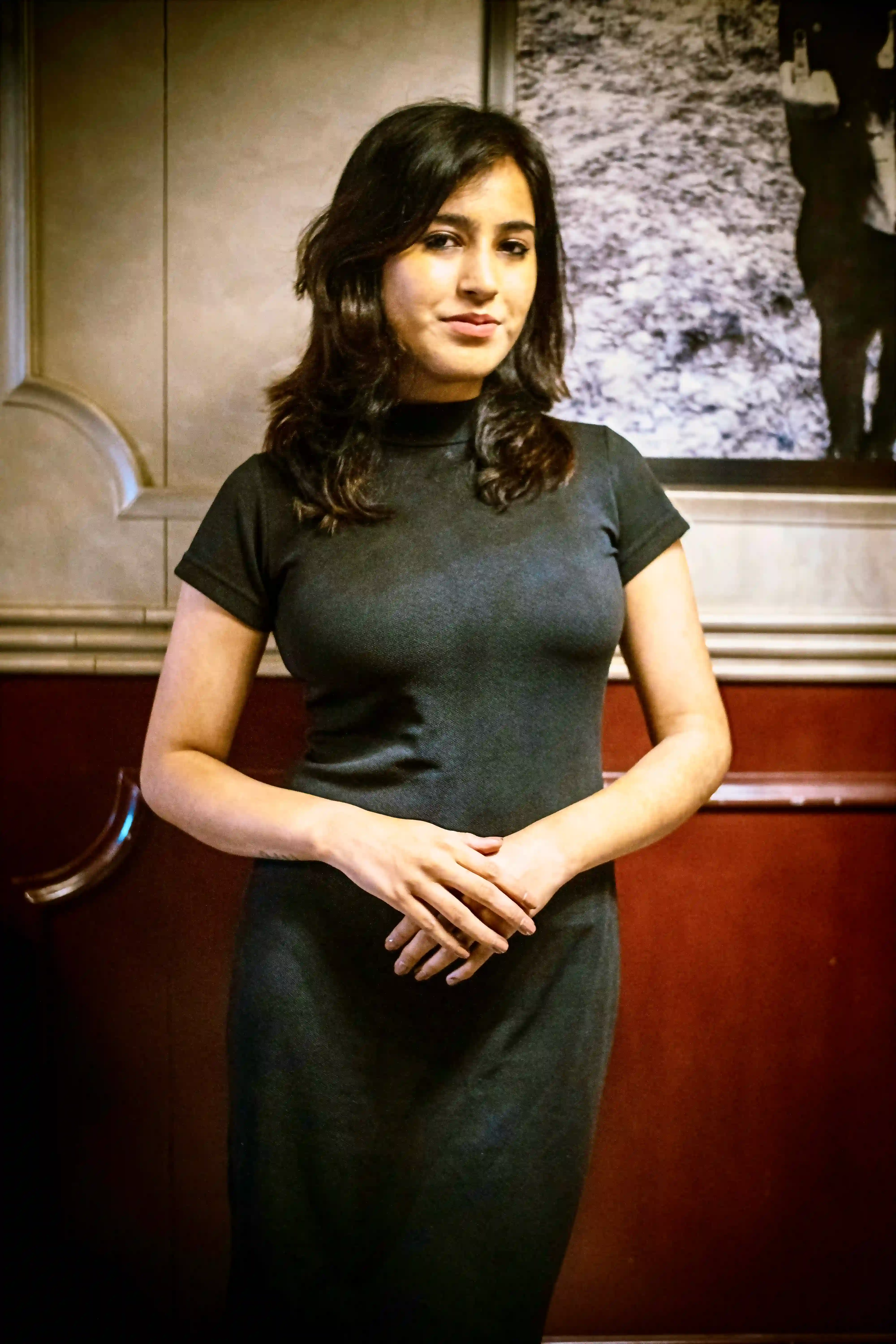 Cover Page sophisticated waitress in black blazer and top, hand on chin with thoughtful expression, in elegant indoor setting with mirror.