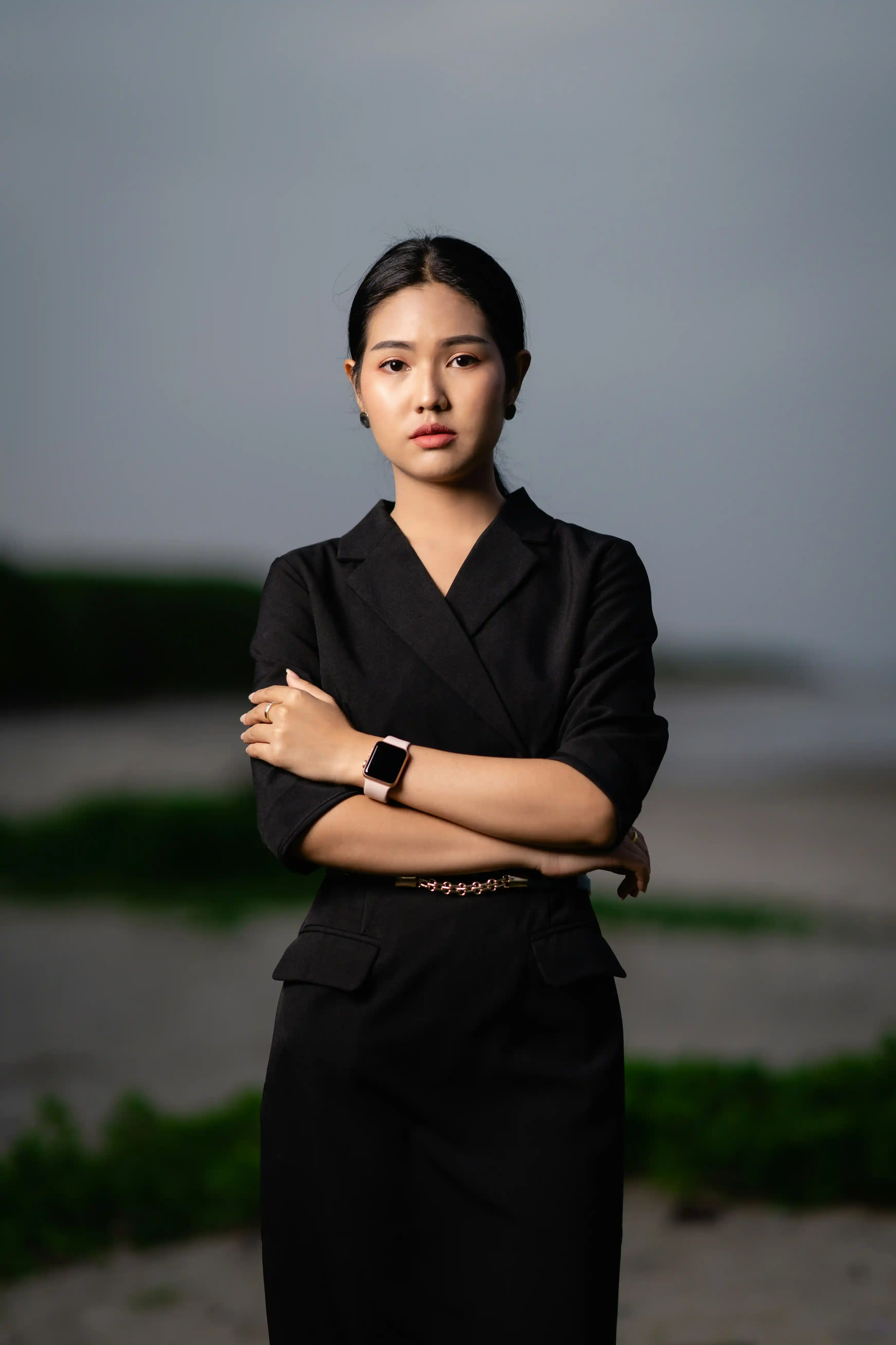 Cover Page professional waitress in black short-sleeve blazer dress and smartwatch, arms crossed in confident pose on outdoor beach landscape.