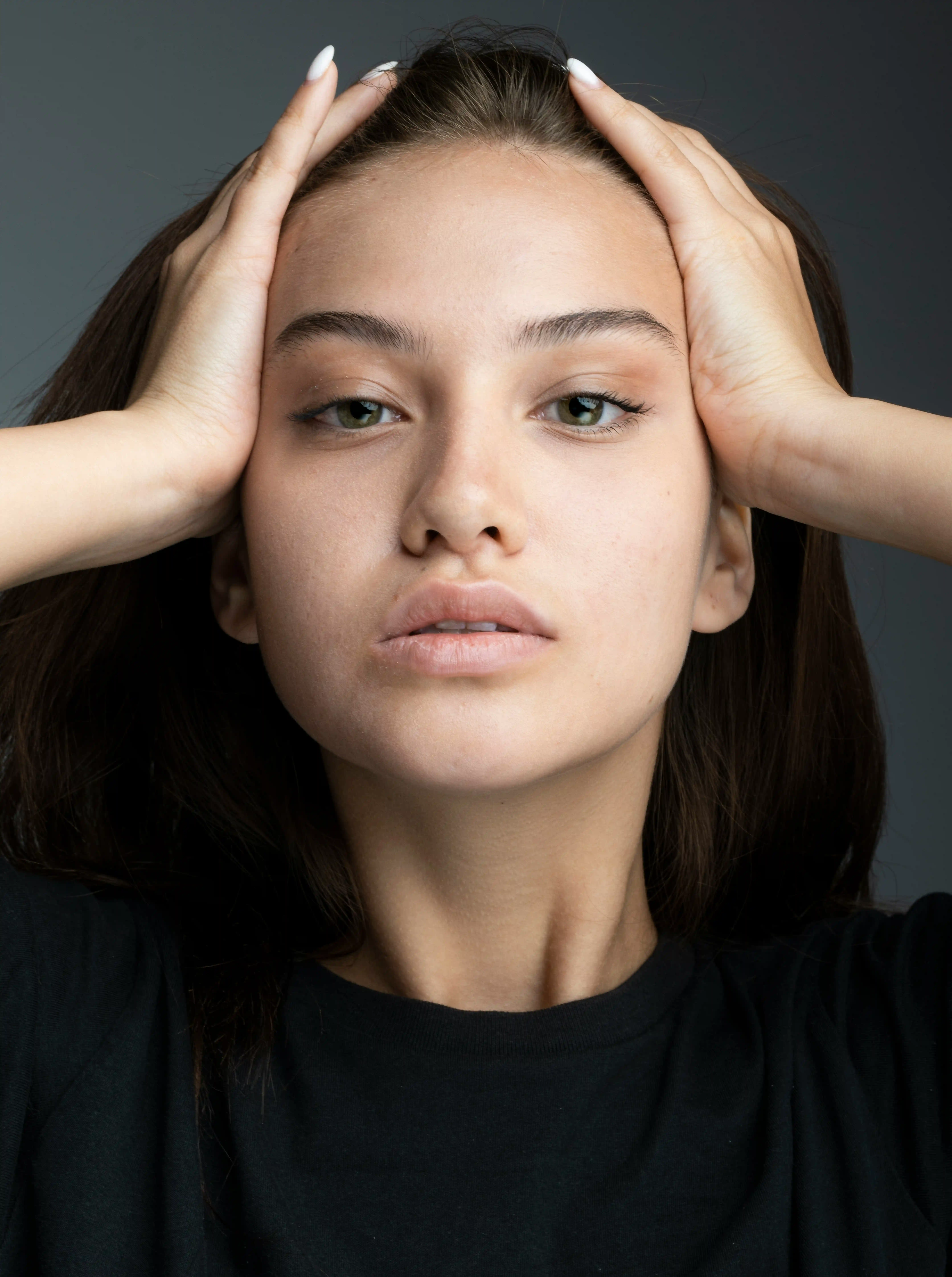 Cover Page model with wet spiked short hair, pink eyeshadow, hand on head in elegant pose on gray background.
