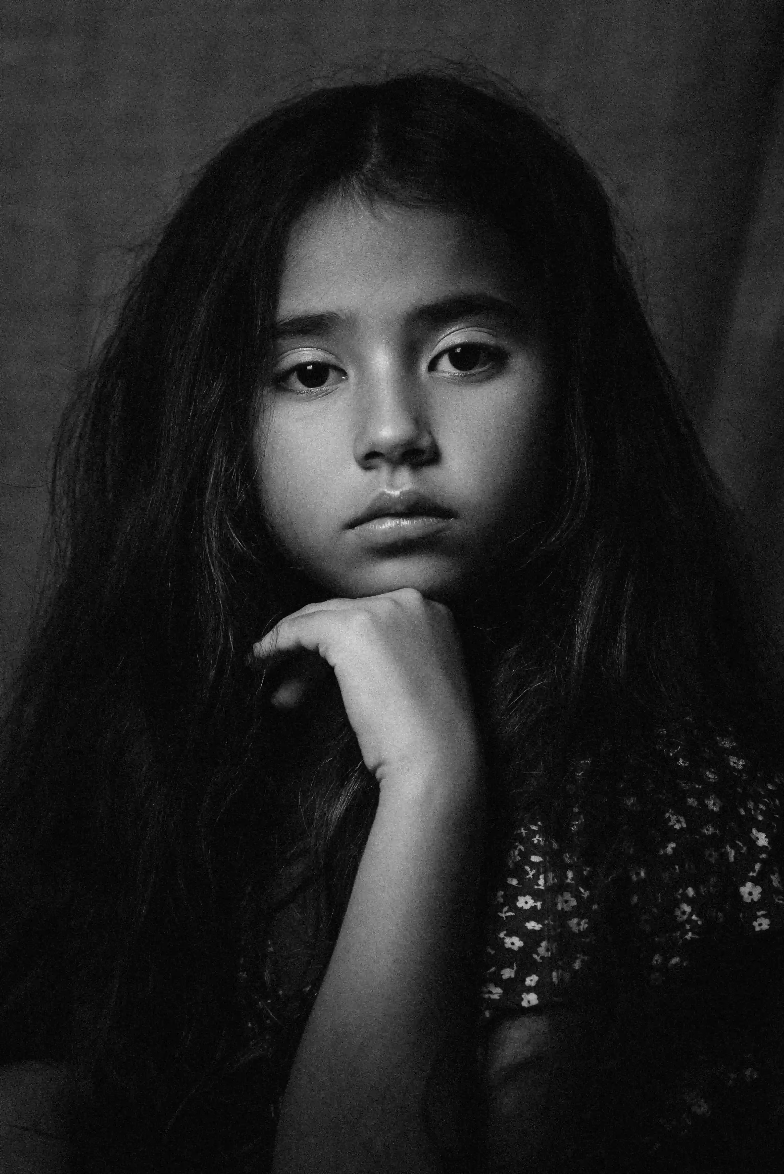 Cover Page young girl in black and white portrait, long hair and floral dress, hand under chin with thoughtful expression on dark background.