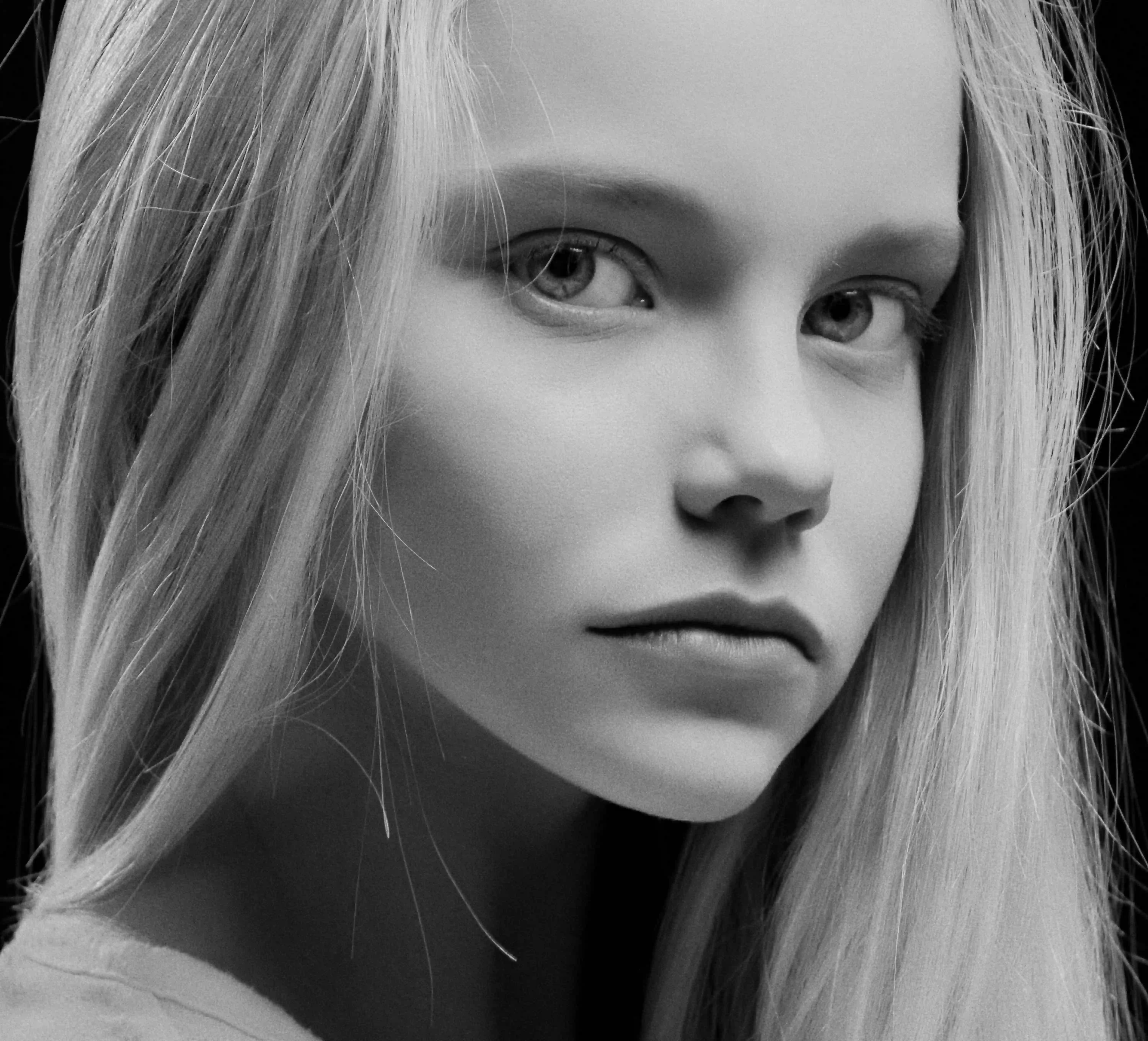 Cover Page young model with long blonde hair, serious expression in side profile, black and white portrait on dark background.