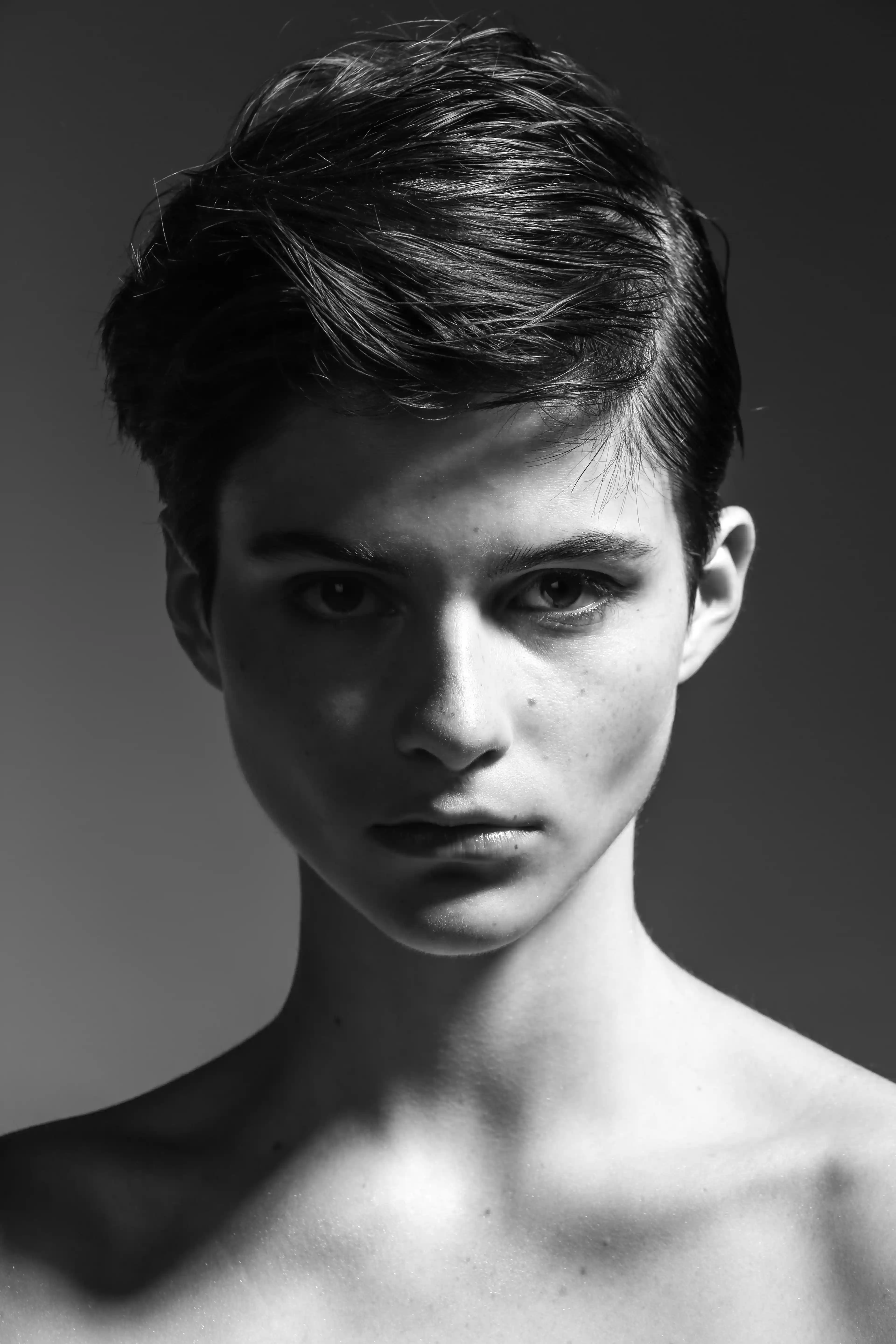 Cover Page young model with short slicked hair, intense gaze and bare shoulders, black and white portrait on gray background.