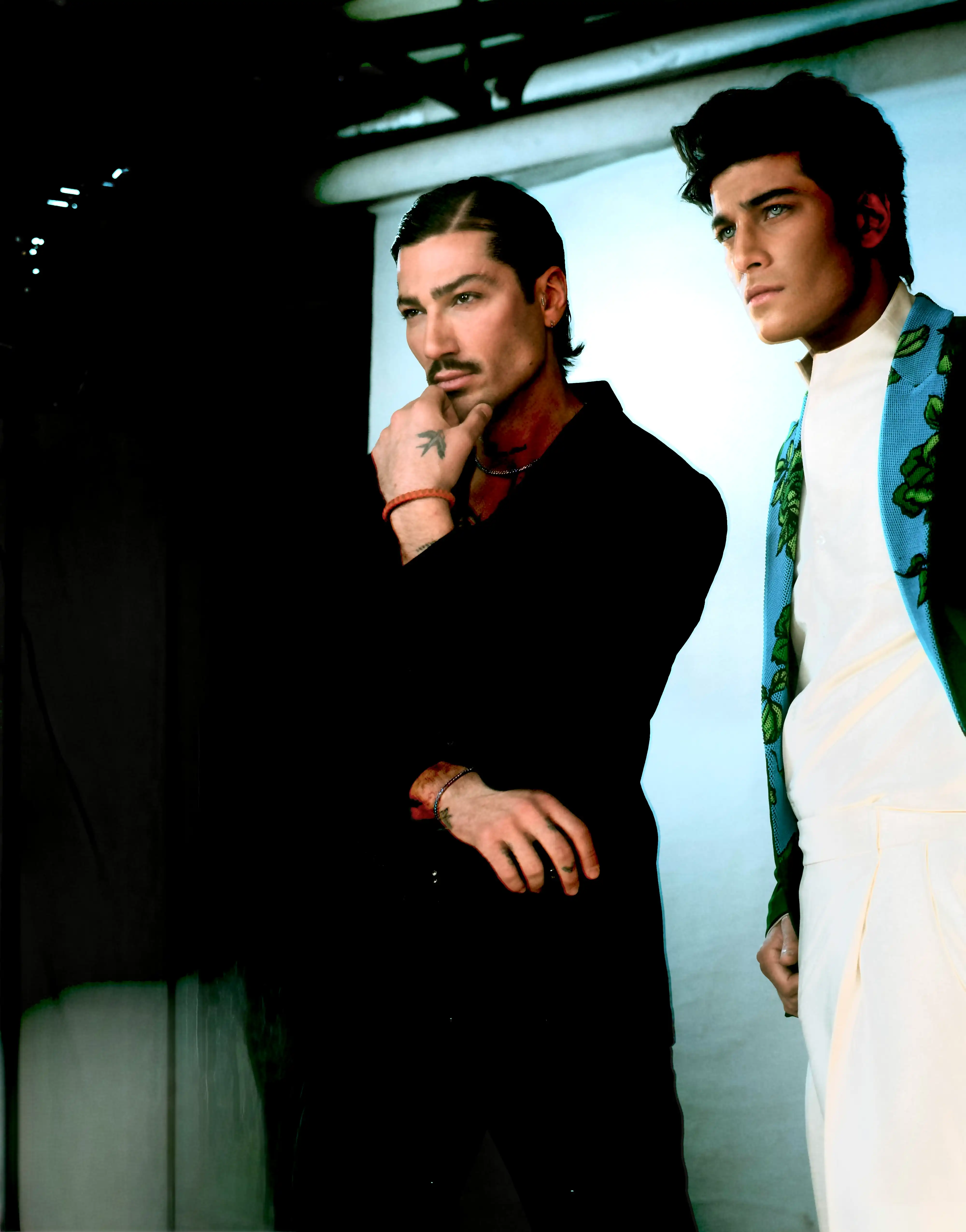 Cover page Dubai: Two male models in a studio, one in a black suit with a mustache and thoughtful pose, the other in a white top with blue and green floral patterns.