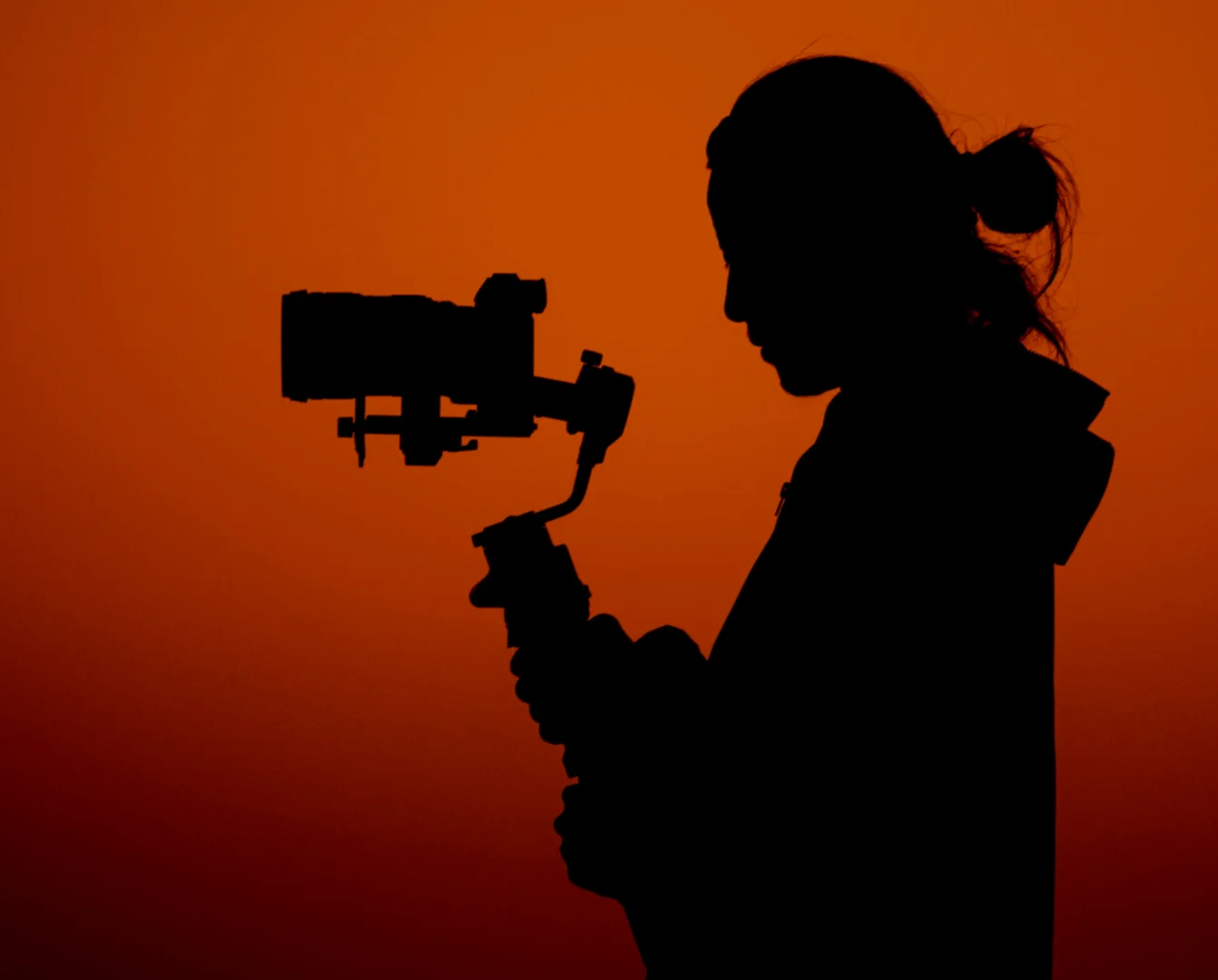 Silhouette of videographer talent holding gimbal camera against orange sunset for Coverpage Dubai luxury event agency.