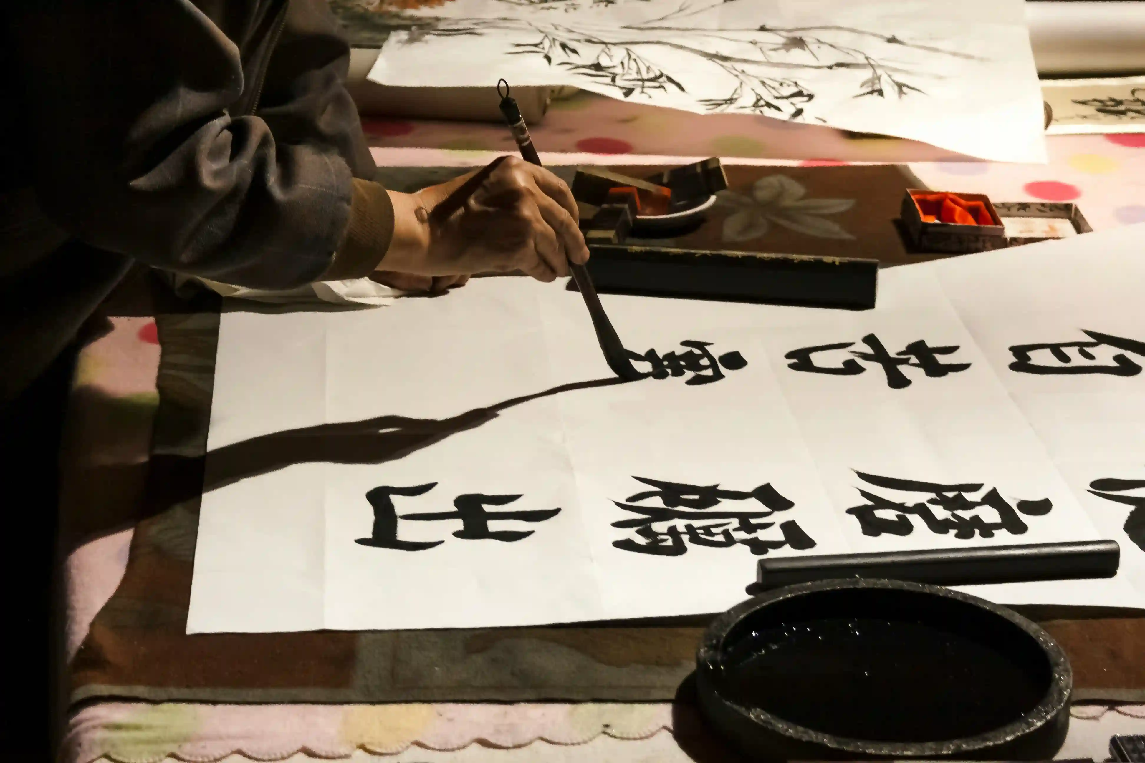 Live Chinese calligraphy artist brushing elegant black ink characters on white paper with traditional brush and inkstone, focused hand in warm ambient light, cultural entertainment for luxury Dubai events, weddings and corporate gatherings 2026
