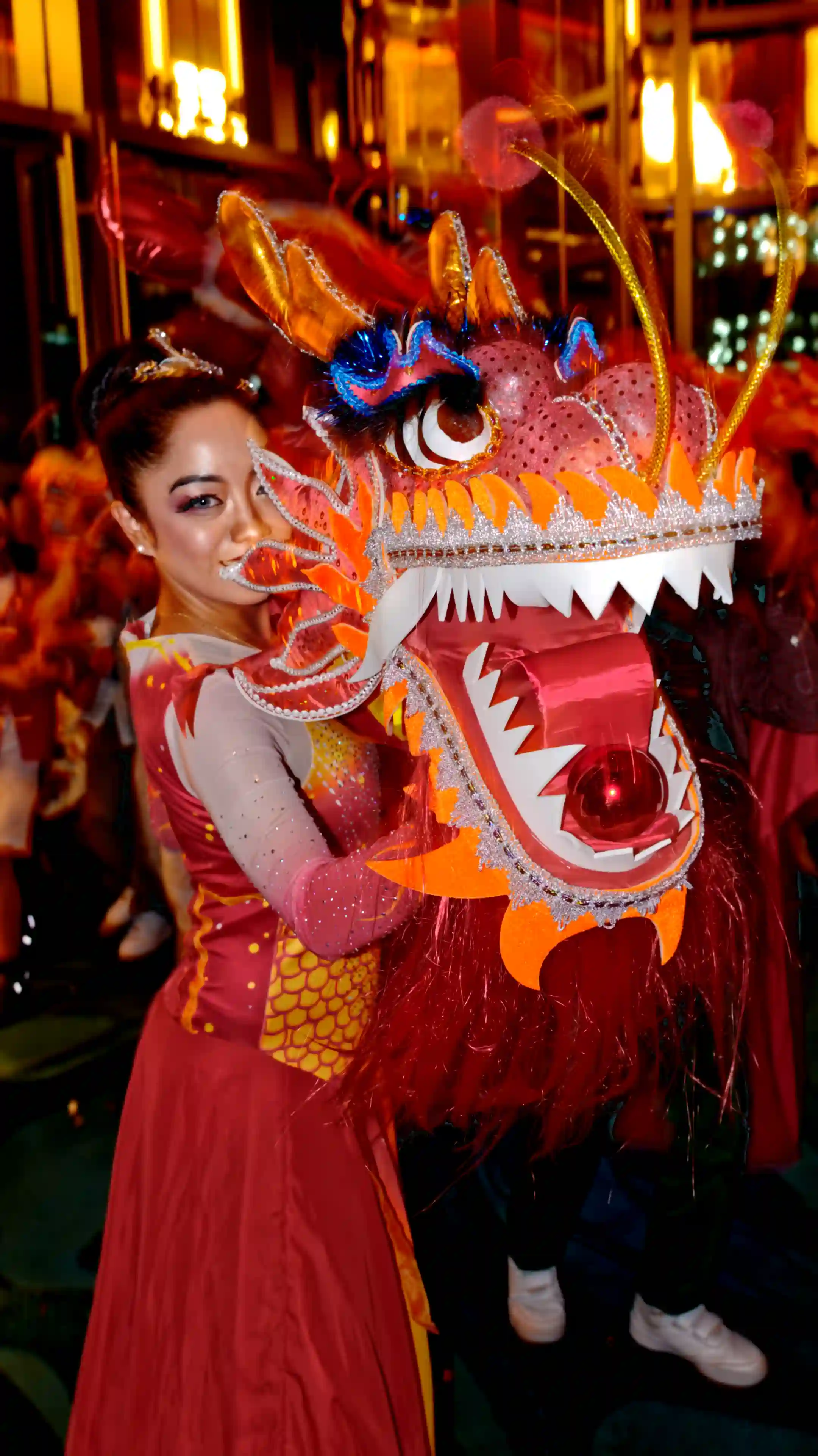 Smiling female Chinese dragon dance performer in vibrant red costume holding large illuminated dragon head, festive lanterns background, traditional live entertainment for Dubai Chinese New Year, corporate events, weddings and luxury parties 2026