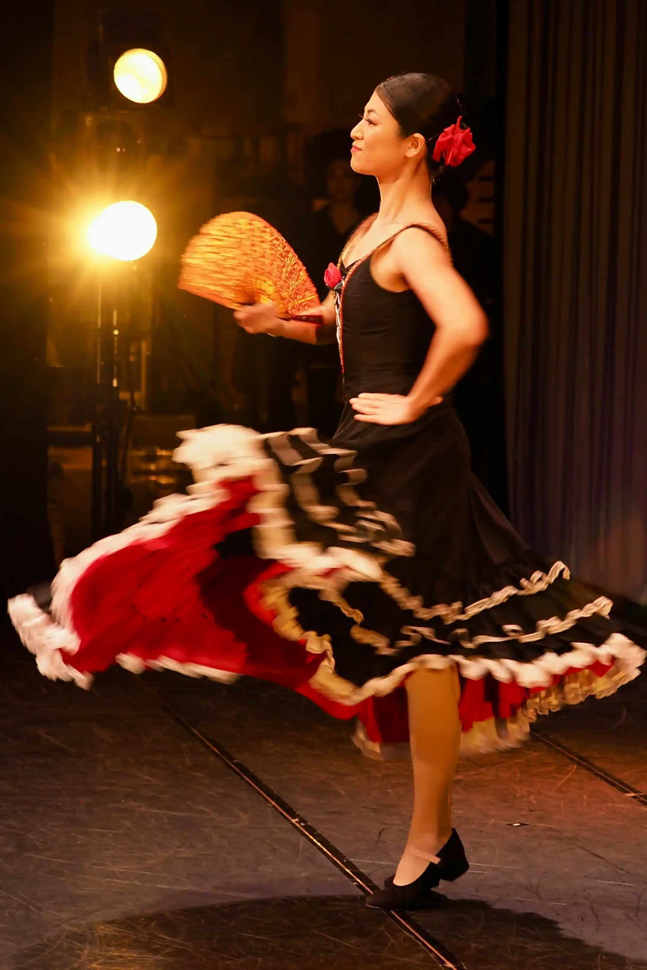 Elegant flamenco dancer in black and red ruffled gown twirling passionately with red fan on stage under warm spotlights, dynamic Spanish cultural dance performance for Dubai luxury events, weddings, corporate galas and dinner shows 2026