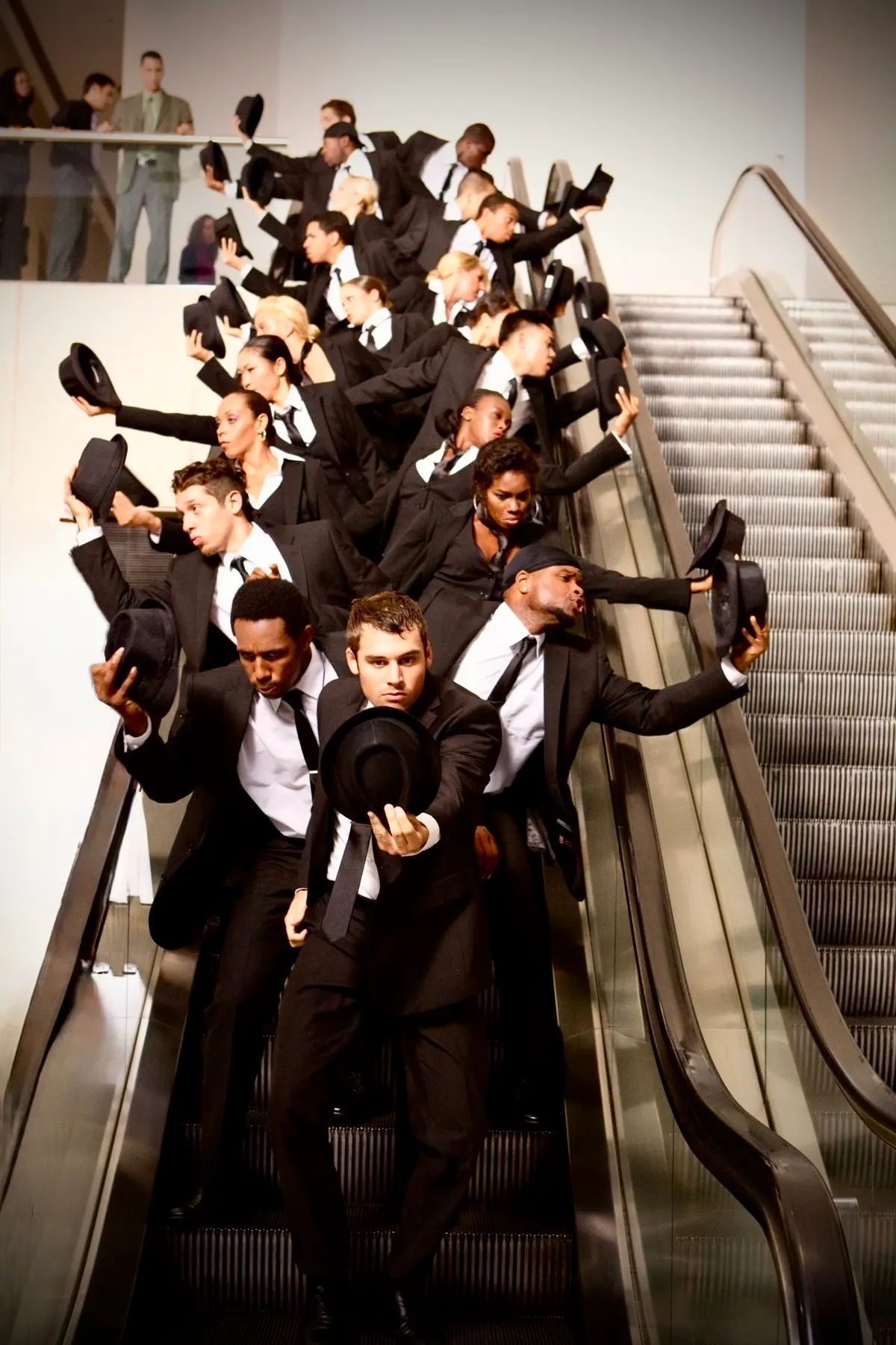 Large synchronized flash mob on escalator with performers in black suits and hats striking dramatic poses, high-energy surprise dance act for Dubai luxury events, corporate activations, weddings, proposals and mall promotions 2026