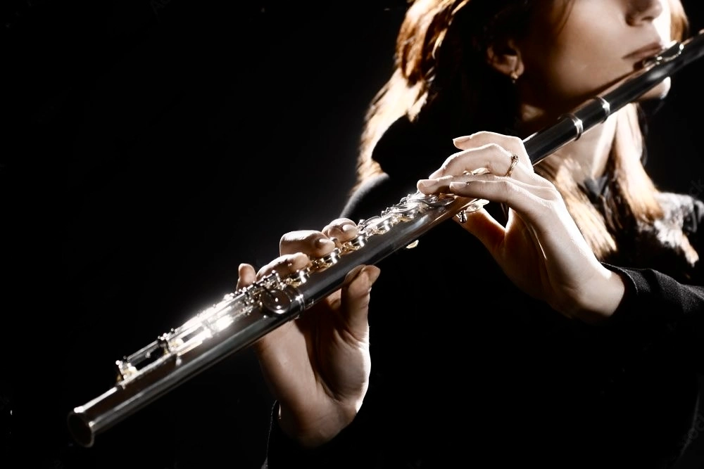 Elegant female flutist playing silver flute in dramatic low-key lighting, close-up on focused hands and instrument, romantic live classical music performance for Dubai luxury events, weddings, corporate galas and hotel entertainment 2026