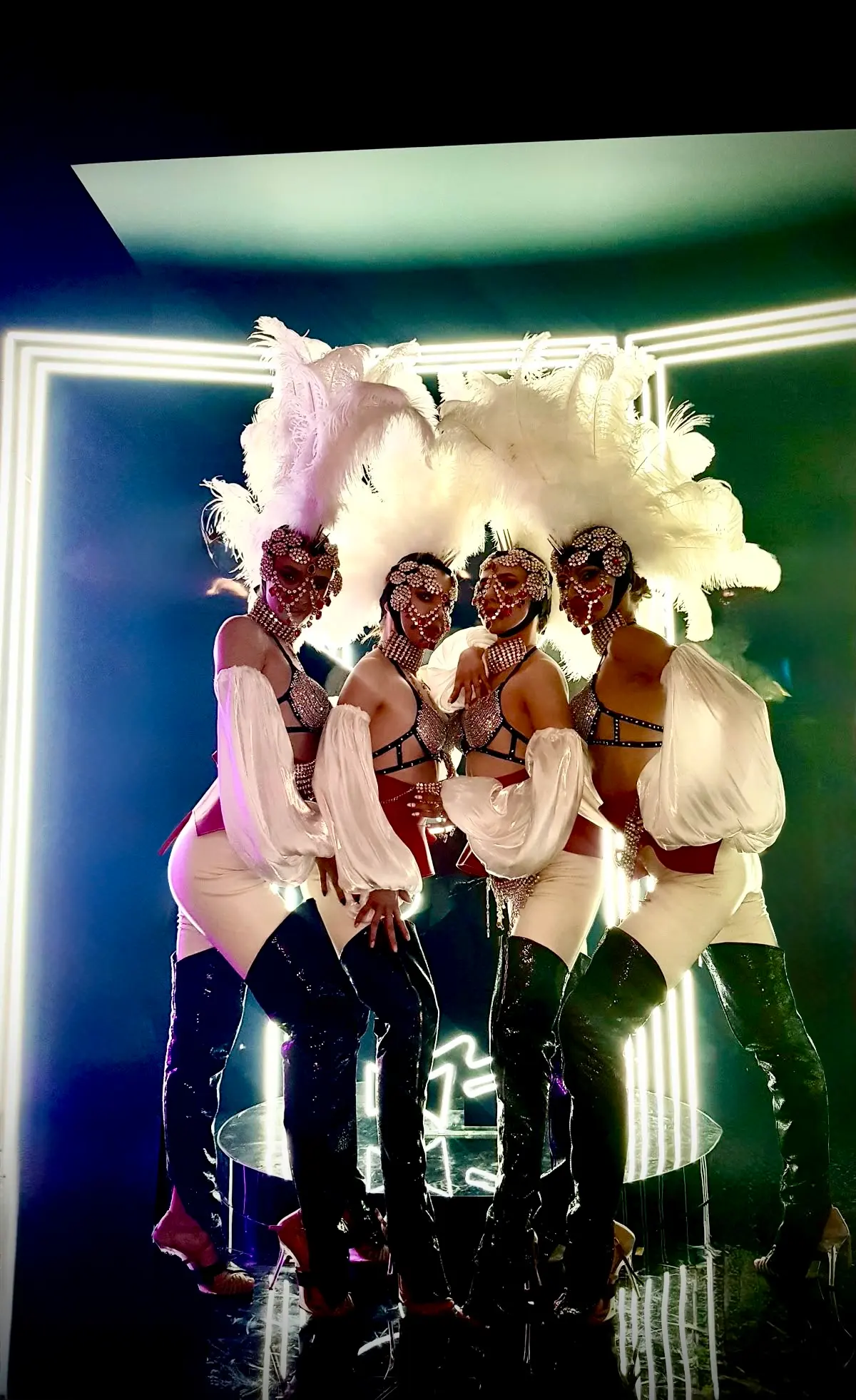 Stunning group of go-go dancers in sparkling sequined outfits, oversized white plumes, flowing sleeves, and bold poses on stage. Luxury entertainment production by Cover Page Agency in Dubai, ideal for high-end parties, corporate events, and club activations.