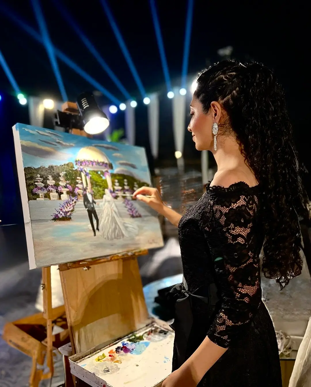 Elegant luxury live painter in a sophisticated black lace gown creating a romantic wedding scene on canvas during an exclusive event for Cover Page Agency Dubai. High-end artistic entertainment talent delivering real-time painting performances at luxury weddings, galas and private parties across the UAE.
