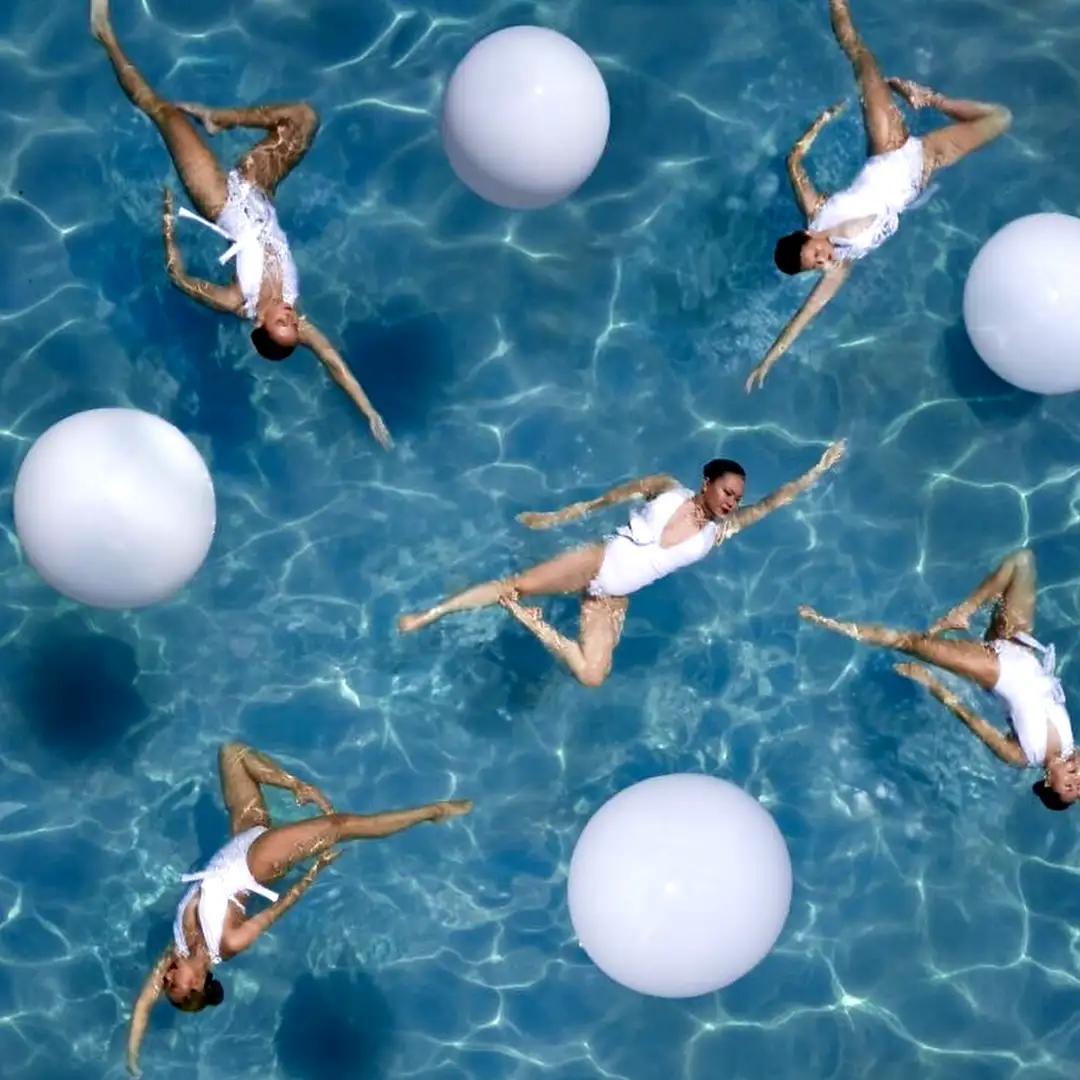 Stunning luxury synchronized swimmers in elegant white costumes creating a breathtaking aerial formation with white balloons in a crystal-clear pool for Cover Page Agency Dubai. High-end aquatic entertainment talent delivering graceful, precise and visually spectacular performances at exclusive pool parties and luxury events across the UAE.