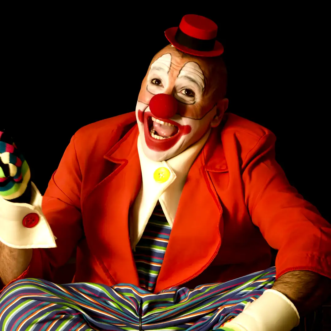 Energetic clown in vibrant red jacket, oversized colorful striped pants, red nose and white face paint, laughing pose with arms wide, classic fun live entertainment for Dubai children's parties, birthdays, family events and corporate activations 2026