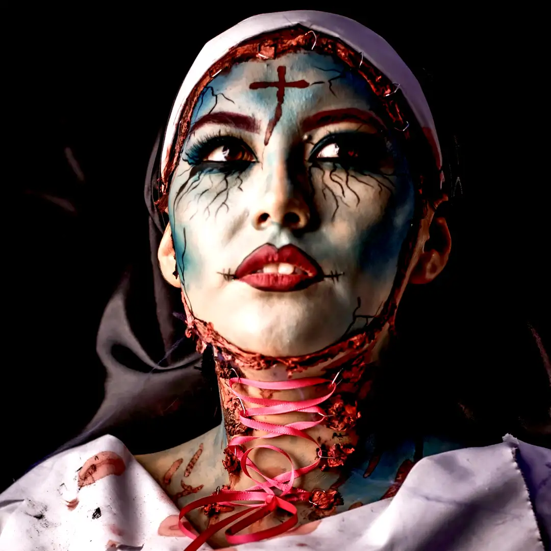 Terrifying evil nun in possessed horror makeup: blue cracked skin, stitched forehead cross, black veins, red lips, and pink ribbon-laced bloody neck. Dramatic close-up performance by Cover Page Agency Dubai. Ideal for Halloween events, themed parties, luxury nightlife, and spooky activations in UAE.