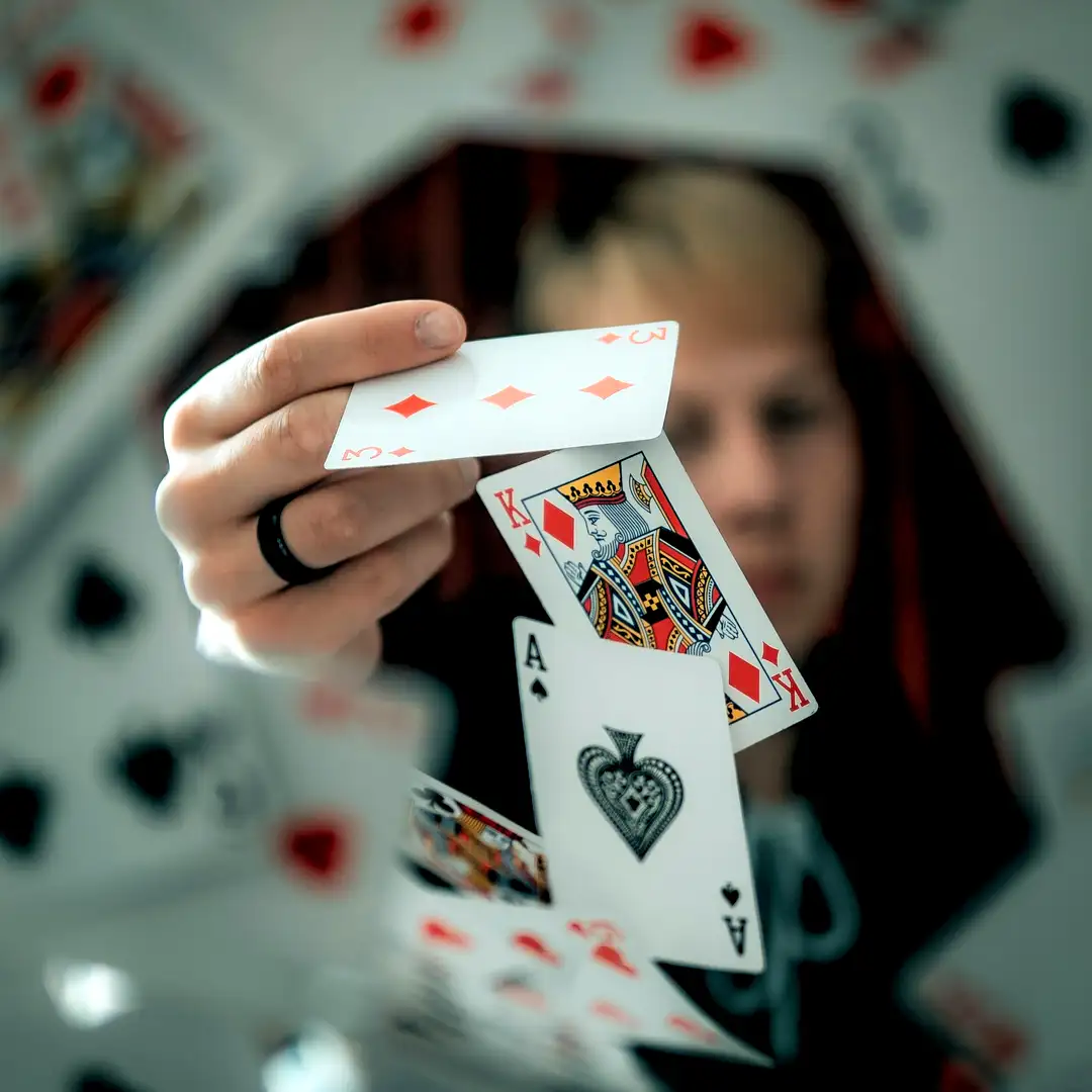 Close-up magician performing card manipulation in an infinity mirror room effect, fanning Ace of Spades, King of Hearts, King of Diamonds, and other playing cards with dramatic reflections. Mysterious close-up magic act by Cover Page Agency Dubai. Perfect for luxury events, casino-themed parties, corporate activations, private shows, and high-end entertainment in UAE.