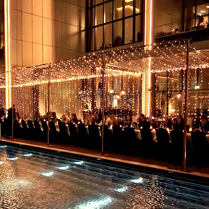 Fairy light structure over a long dinner table beside a rooftop pool at an event in Dubai