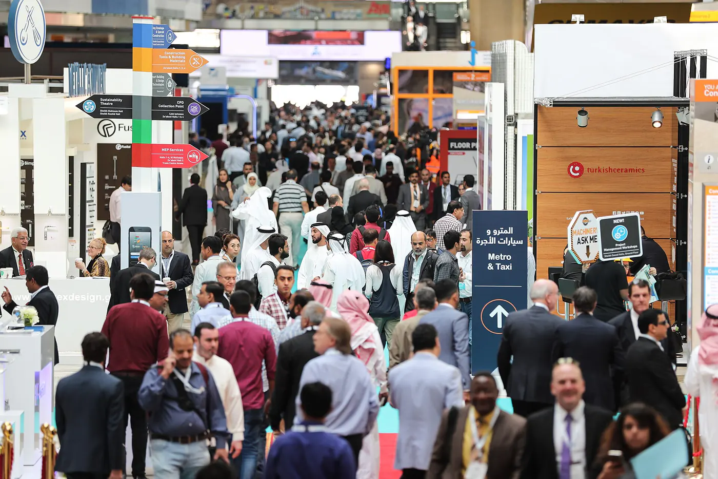 Hostess scanning a visitor badge at a construction expo stand with stone and steel samples in a daylight hall in Dubai