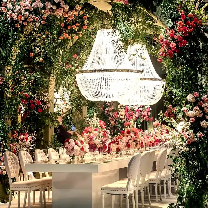 Flower wall and chandelier over a long dinner table at an event