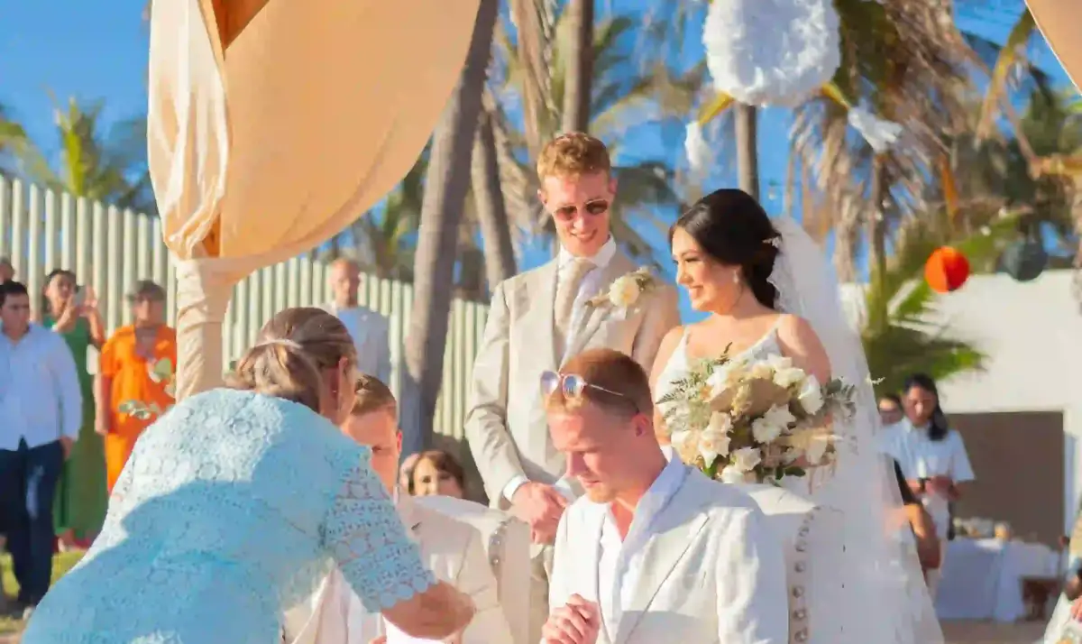 Couple smiling at their beach wedding ceremony under a draped canopy, a guest signing the register