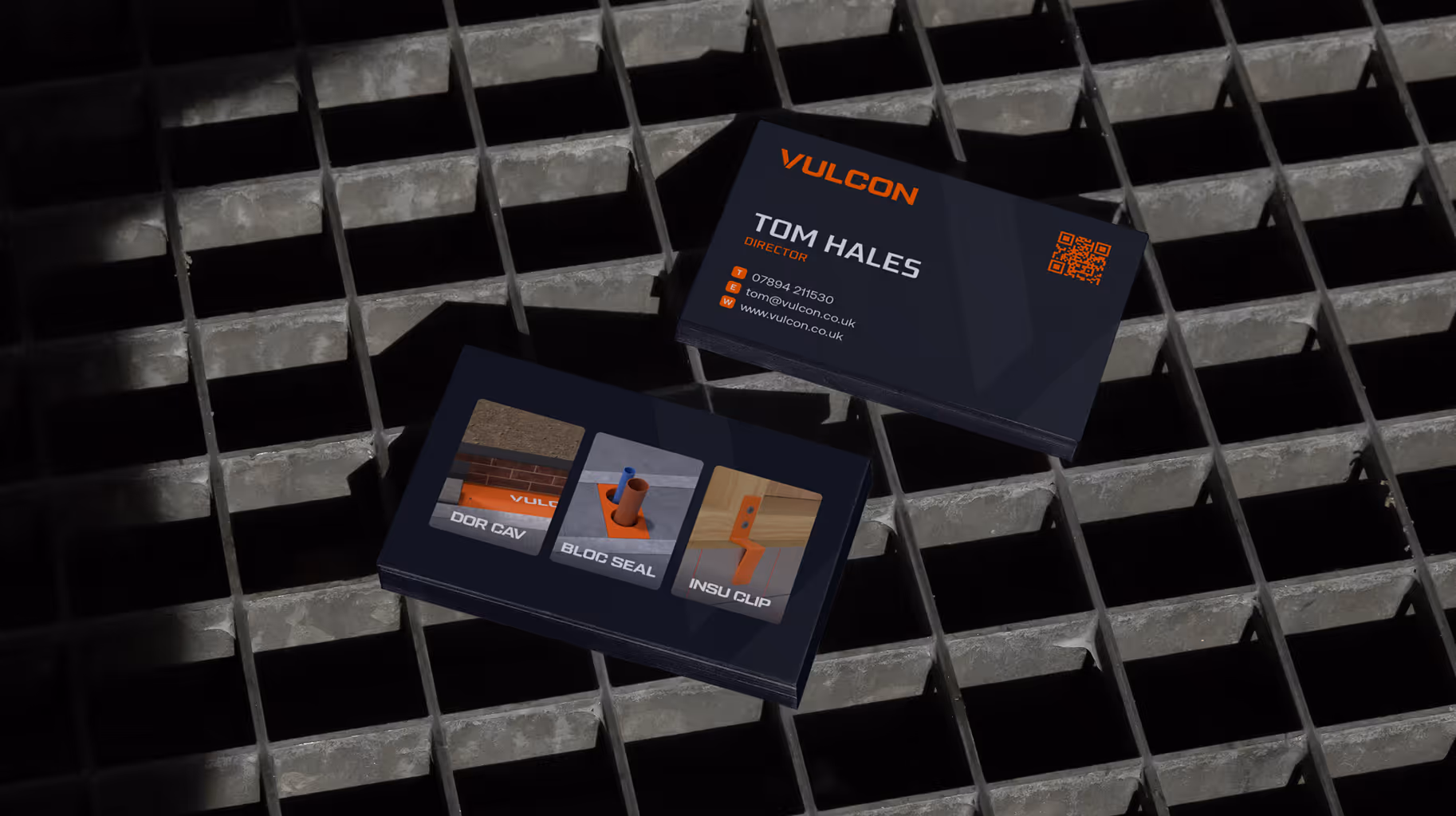 Two dark business cards on metal grate; one with contact info for Tom Hales, director at Vulcon.