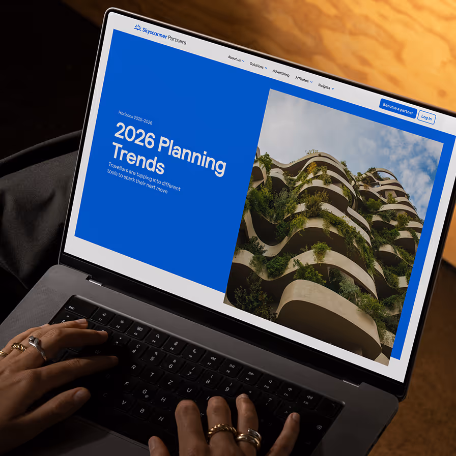 Person typing on laptop displaying Skyscanner page on 2026 Planning Trends with green building image.