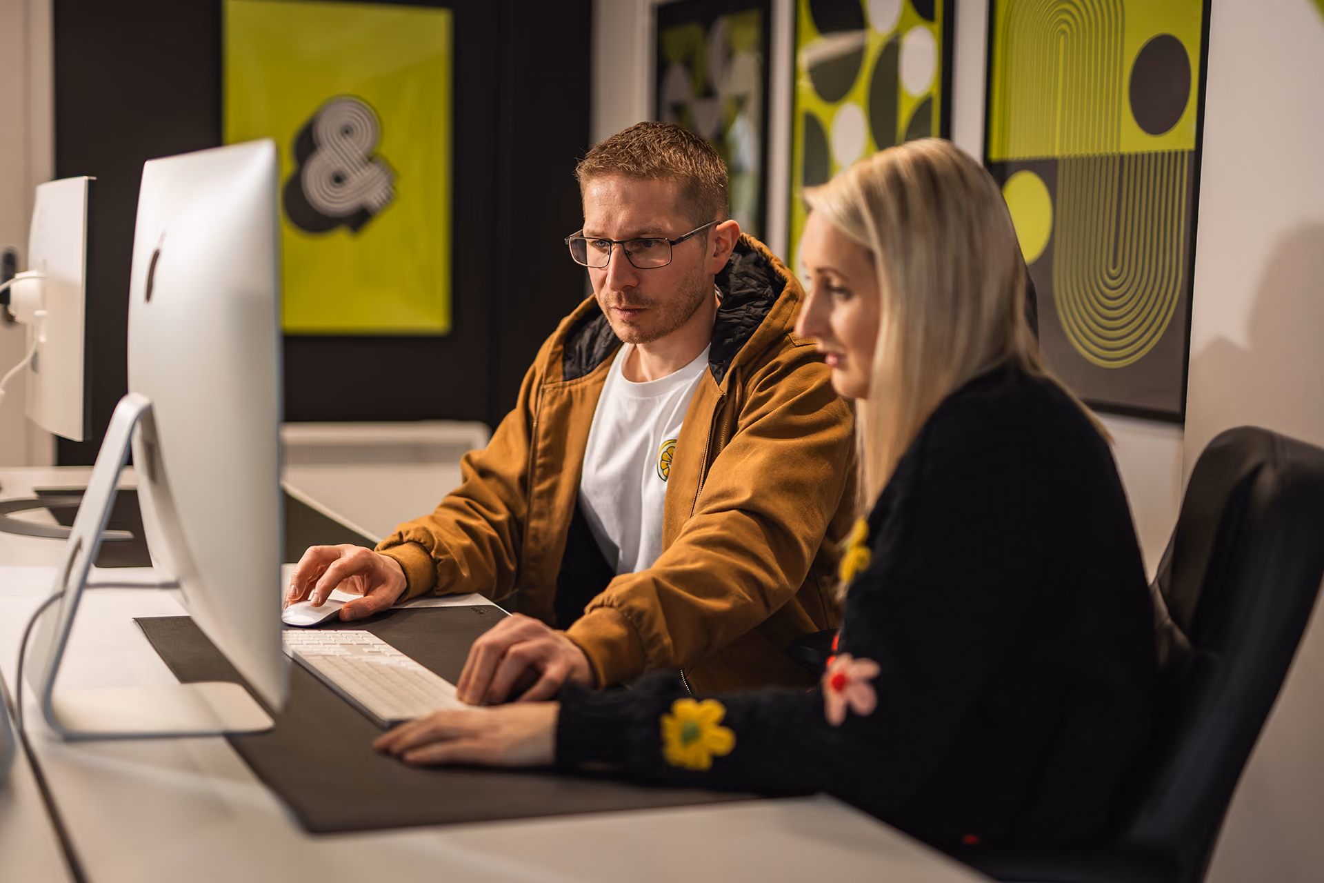 Man and woman working together at a desk using a large computer in a modern office.