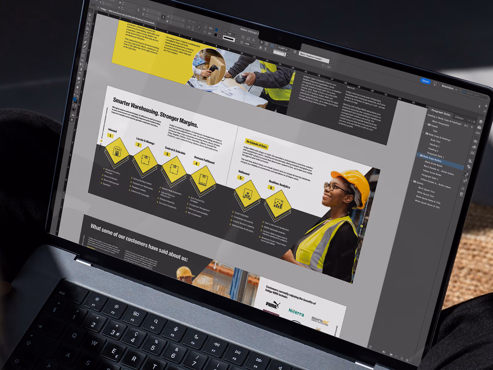 Laptop screen shows a warehouse management brochure design in Adobe InDesign with a worker photo and process icons.