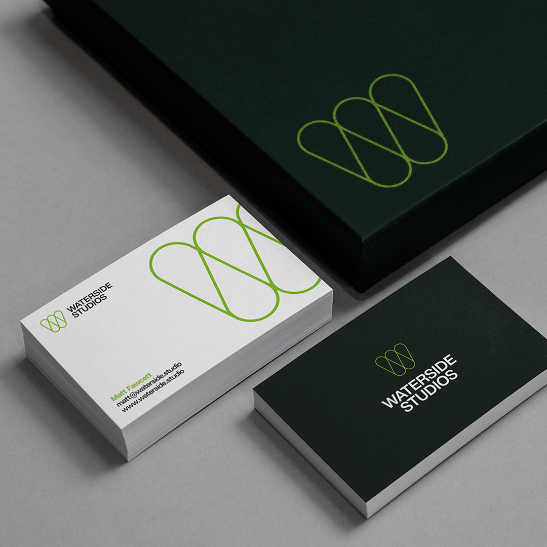 Waterside Studios business cards and box with green logo and black and white design on gray background.