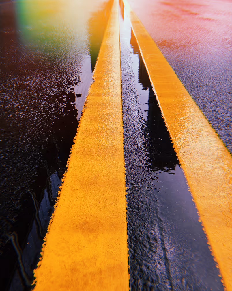 Close-up of two parallel yellow road lines on wet asphalt reflecting light.