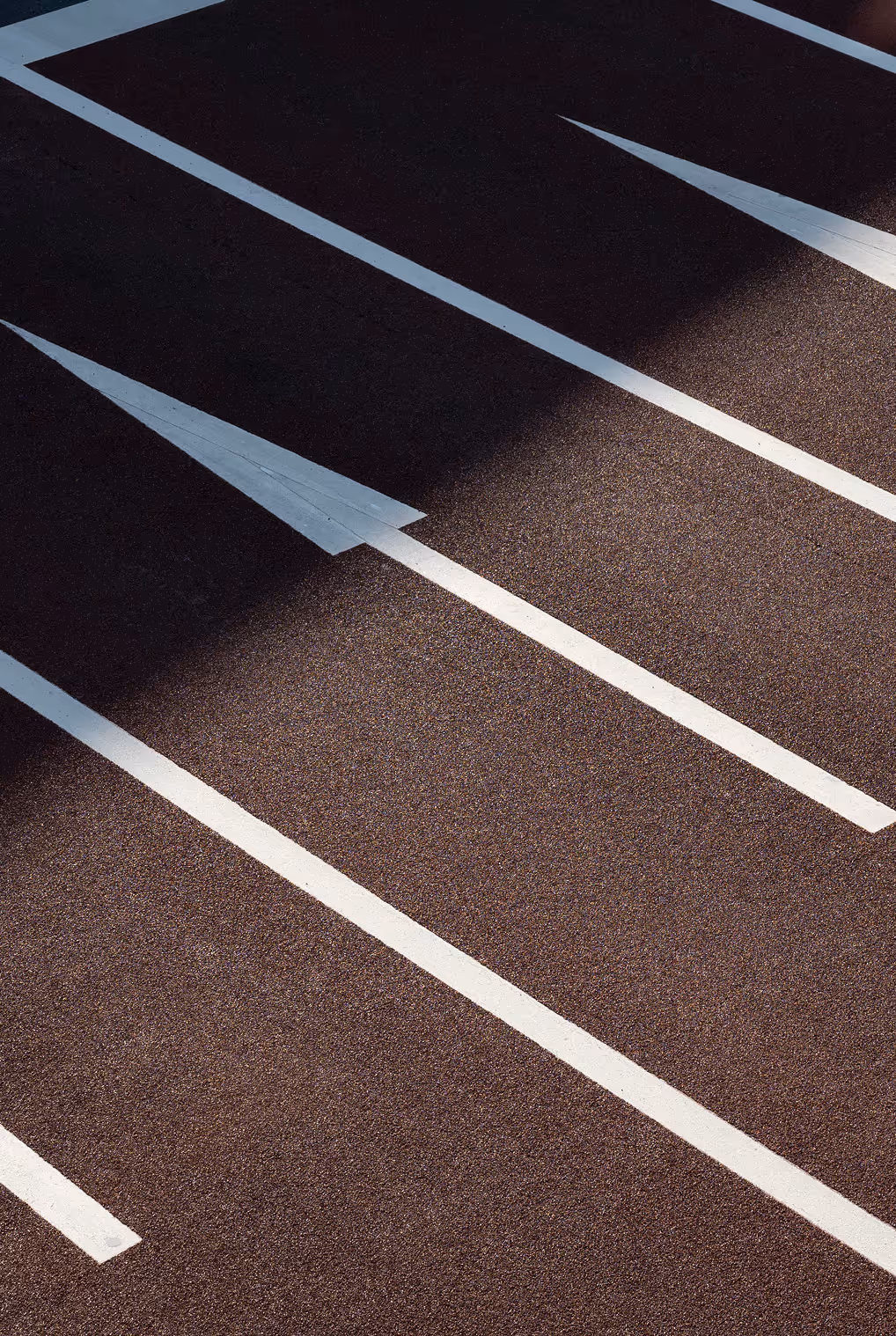 Empty asphalt parking spaces with white directional arrows and shadow crossing diagonally.