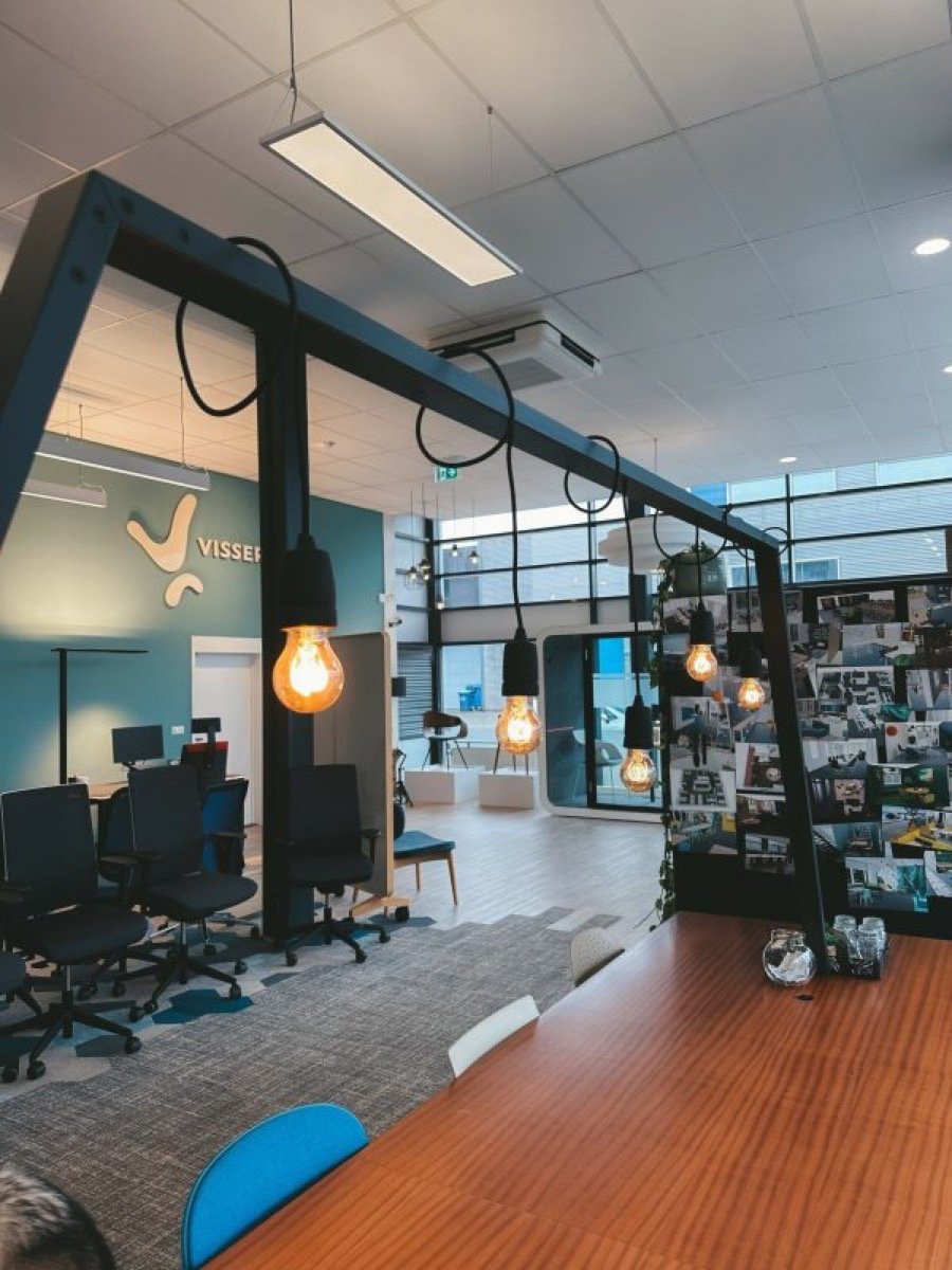 Moderne kantoorruimte met ophanglampen, bureaustoelen, grote tafel en fotomuur.