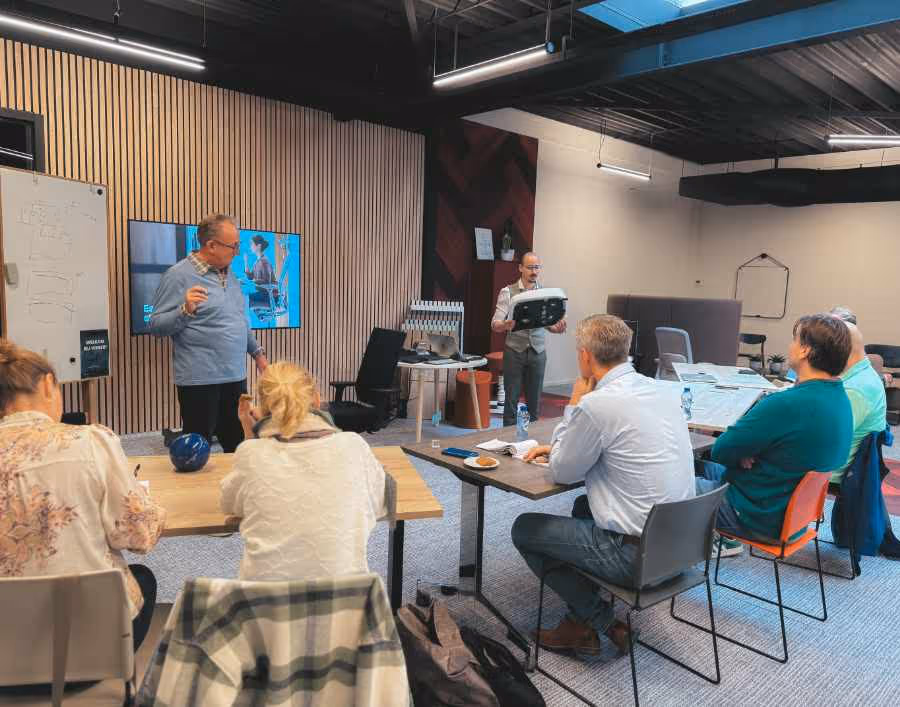 Groep volwassenen luistert naar twee mannen die lesgeven in een moderne klasruimte.