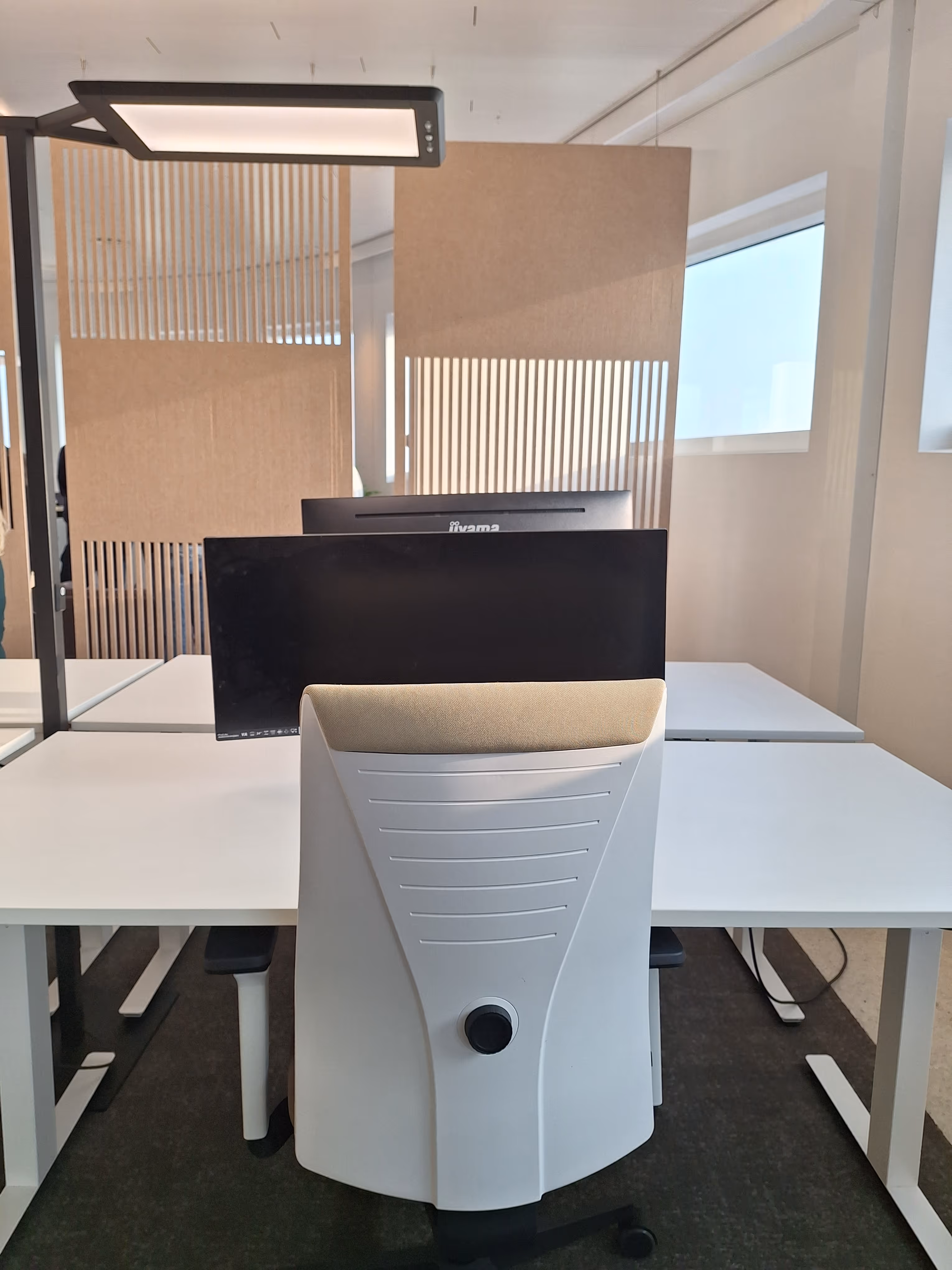 Witte bureaustoel met beige hoofdsteun voor een computerscherm op een wit bureau in een kantoor.