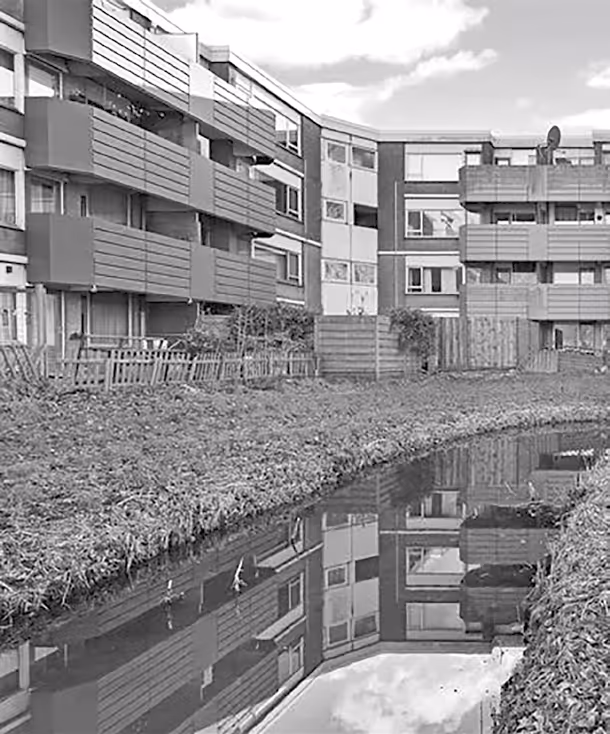 Appartementengebouwen met balkons weerspiegeld in een smalle waterpartij onder een partly bewolkte lucht.