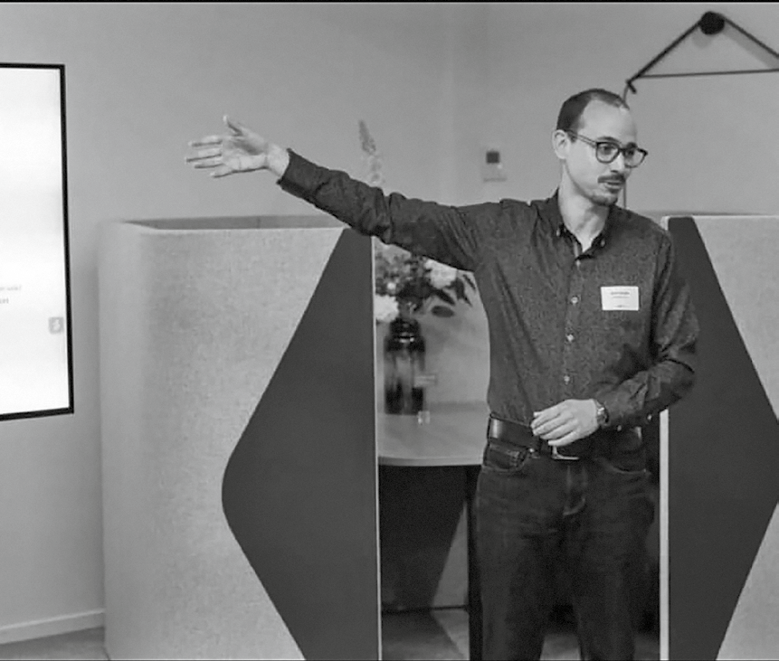 Man met bril die tijdens presentatie met uitgestrekte arm naar scherm wijst.