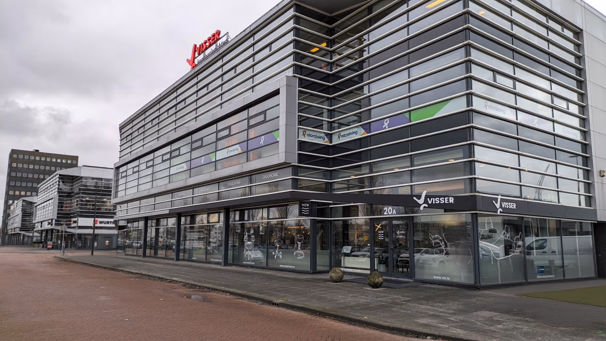 Moderne kantoorgebouw met grote ramen en Visser bedrijfsnaam op gevel aan een brede stoep.