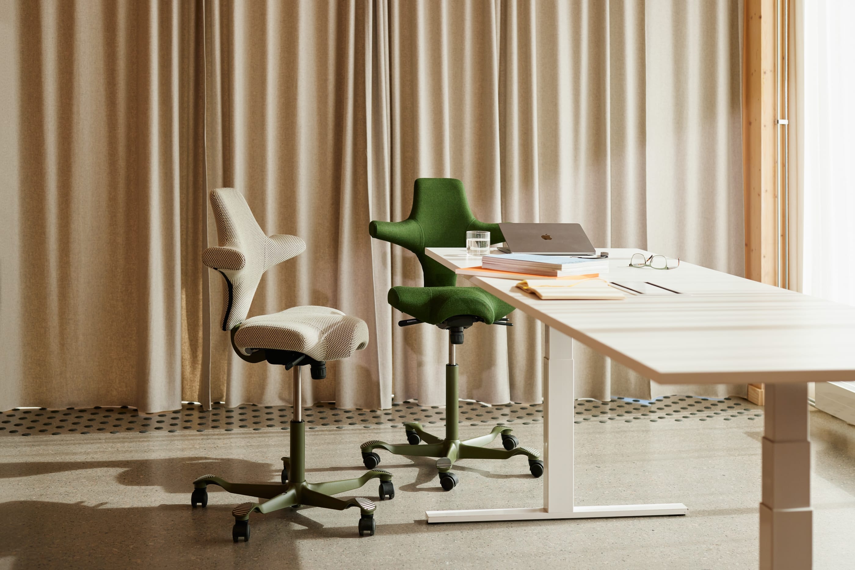 Moderne kantoorruimte met een witte verstelbare tafel en twee ergonomische stoelen, één groen en één grijs.